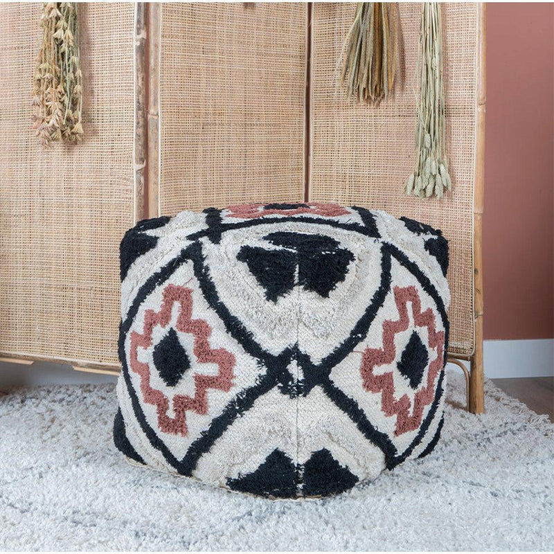 Wollen poef met geometrisch patroon in zwart, wit en bruin, geplaatst op beige vloerbedekking.