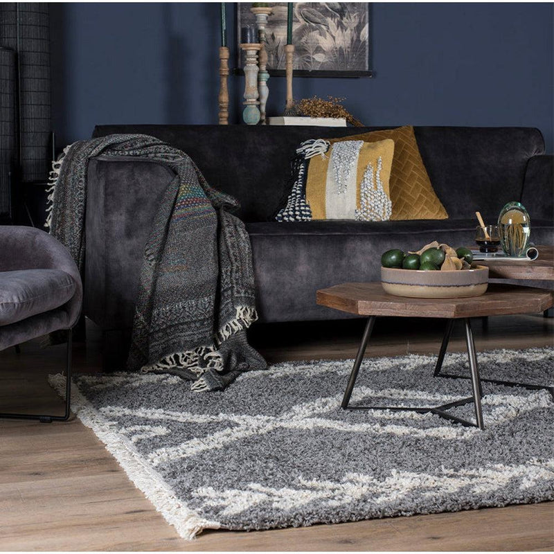 Stijlvolle woonkamer met donkergrijze bank, kleurrijke kussens, houten tafel en modern grijs-wit kleed.