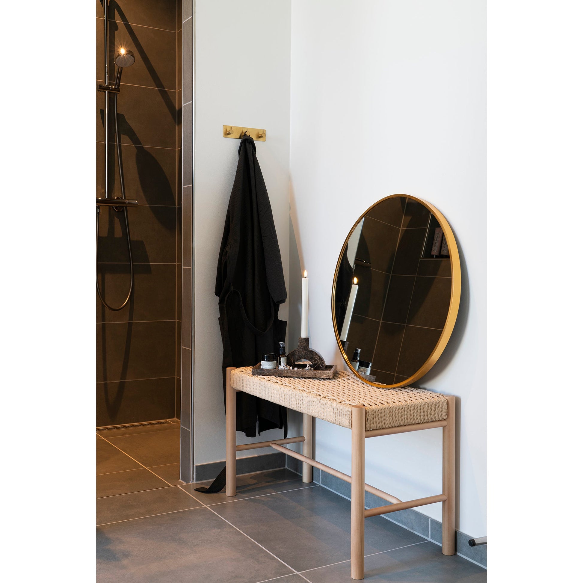 Ronde spiegel met gouden rand, kaarsen en decoratie op geweven bankje in stijlvolle, moderne badkamer.