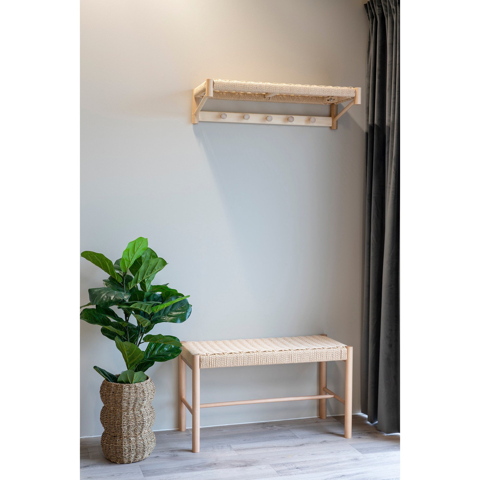 Moderne hal met houten bankje, wandplank met haken en groene plant in gevlochten mand, lichte muur en vloer.