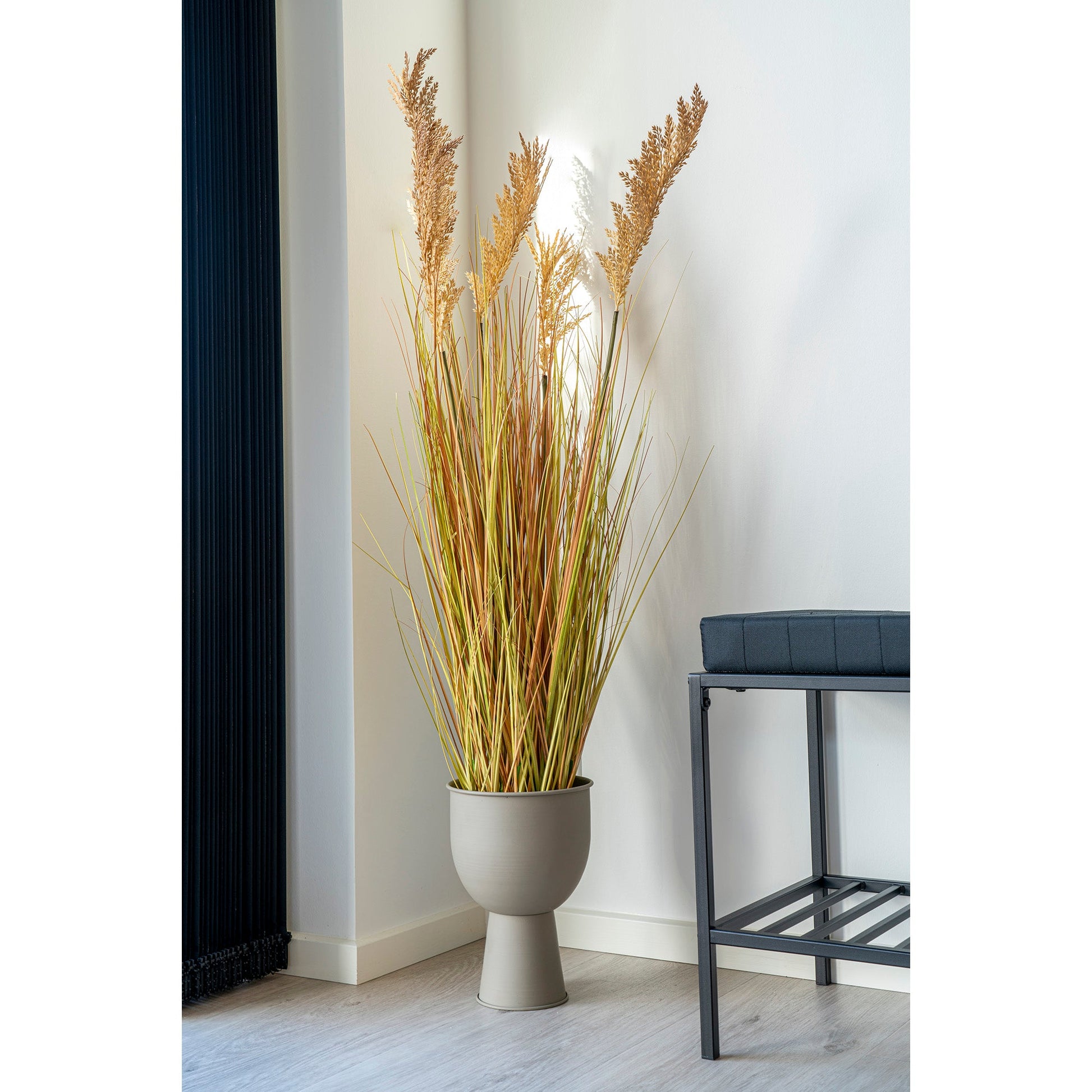 Decoratieve grassen in een beige vaas, naast een moderne zwarte bank in een minimalistisch ingerichte hoek.