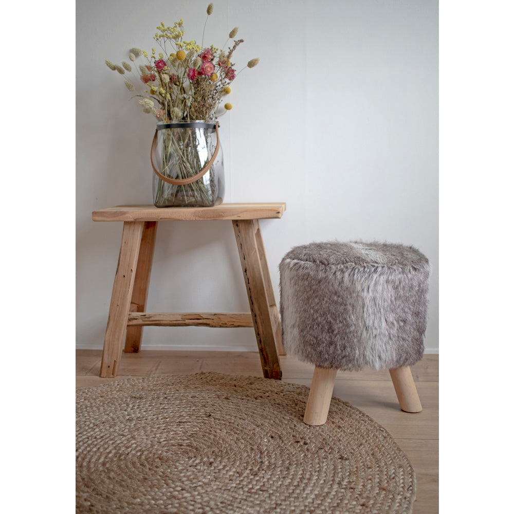Rustiek interieur met houten bankje, vaas met wilde bloemen, pluizige kruk en gevlochten juten tapijt.