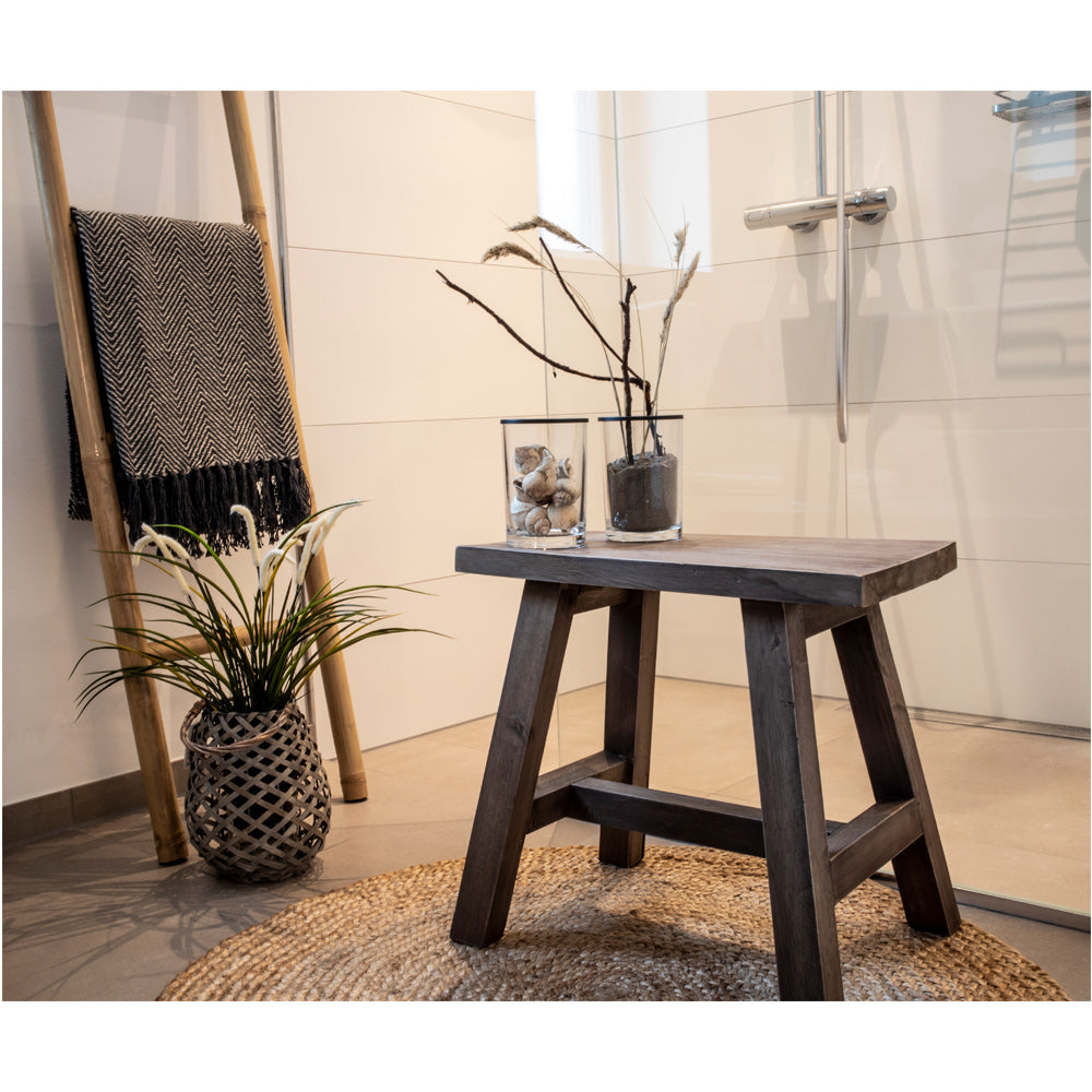 Rustieke badkamer met houten krukje, decoratieve stenen en takken. Grijs gewoven deken op bamboerek.