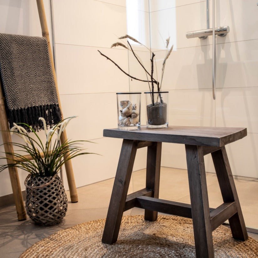 Houten badkamertafel met decoratieve glazen vaten, gevlochten kleed, planten en een doek op een ladder.
