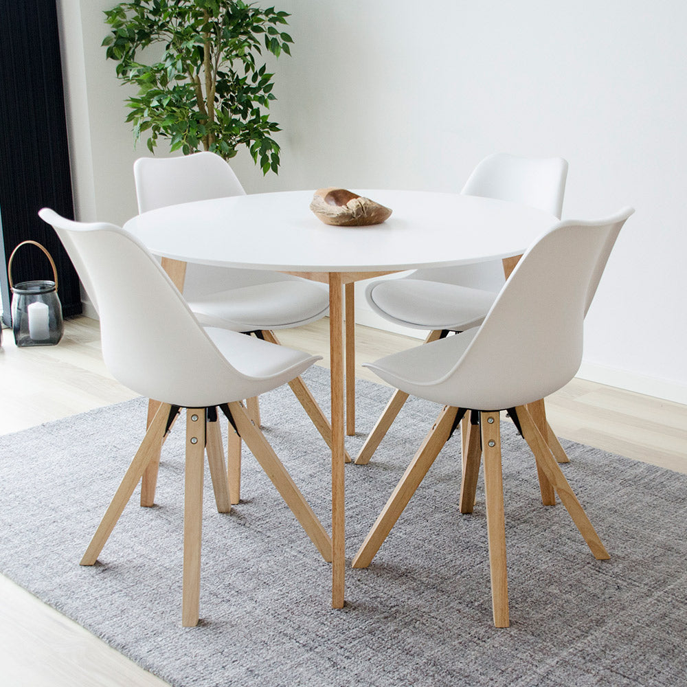 Ronde witte tafel met vier witte stoelen op houten poten, op een grijs tapijt in een minimalistische eetkamer.