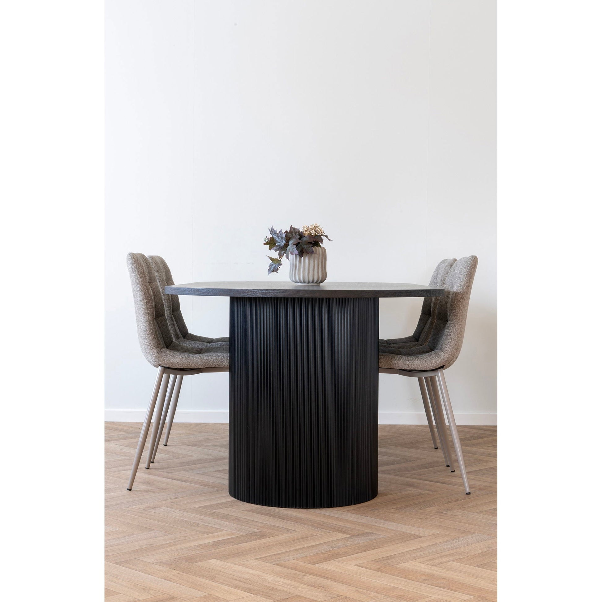 Minimalistische eetkamer met lichtgrijze keramische bloempot Ø15 cm op ronde zwarte tafel, matte geribbelde afwerking als subtiel accent