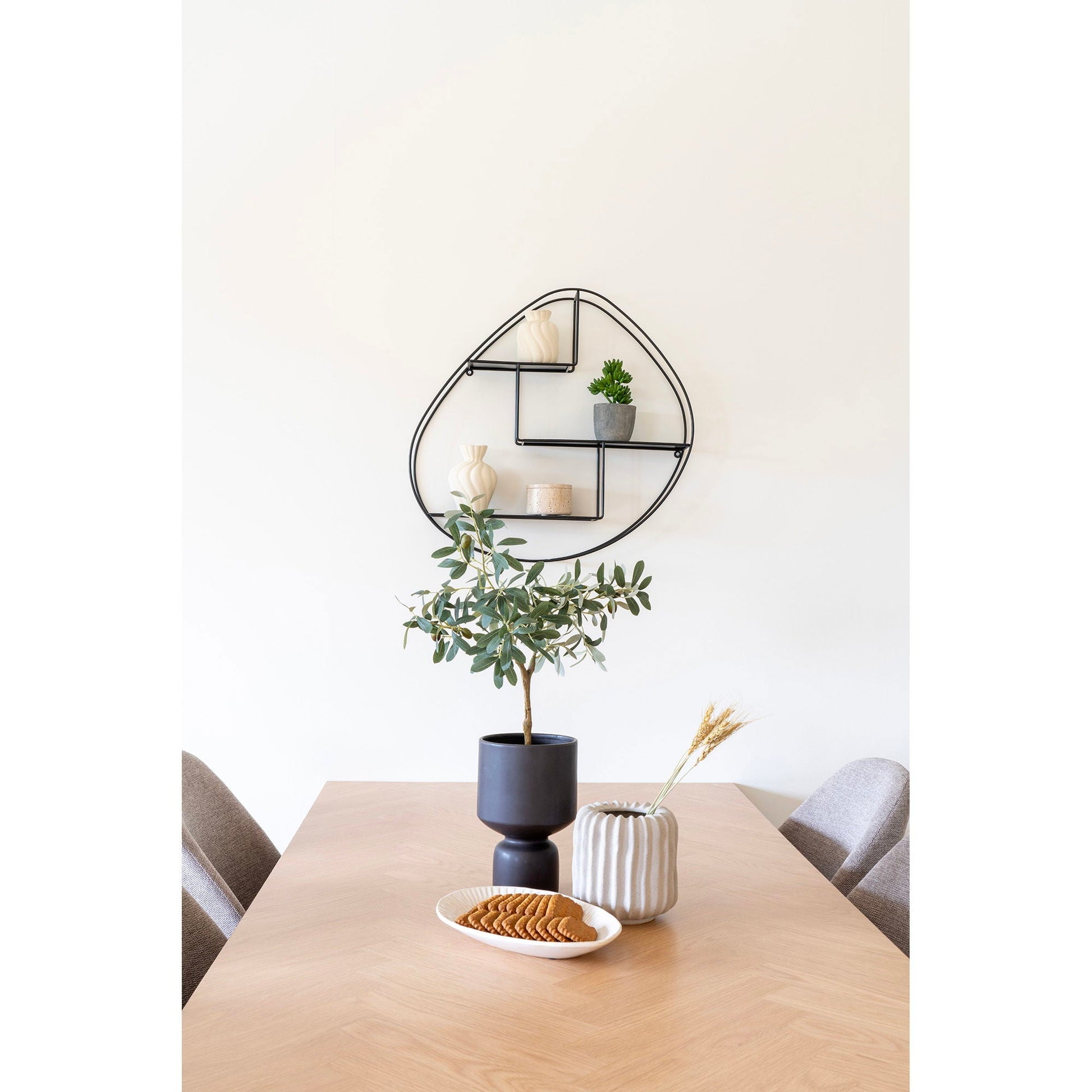 Stijlvolle eethoek met lichtgrijze keramische bloempot Ø15 cm en golvende opening naast zwarte vaas en bord speculaas op eiken tafel