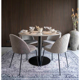 Rond marmeren eettafel met grijze stoelen, gedekte glazen op een sierlijk tapijt, tegen houten lamellenwand.