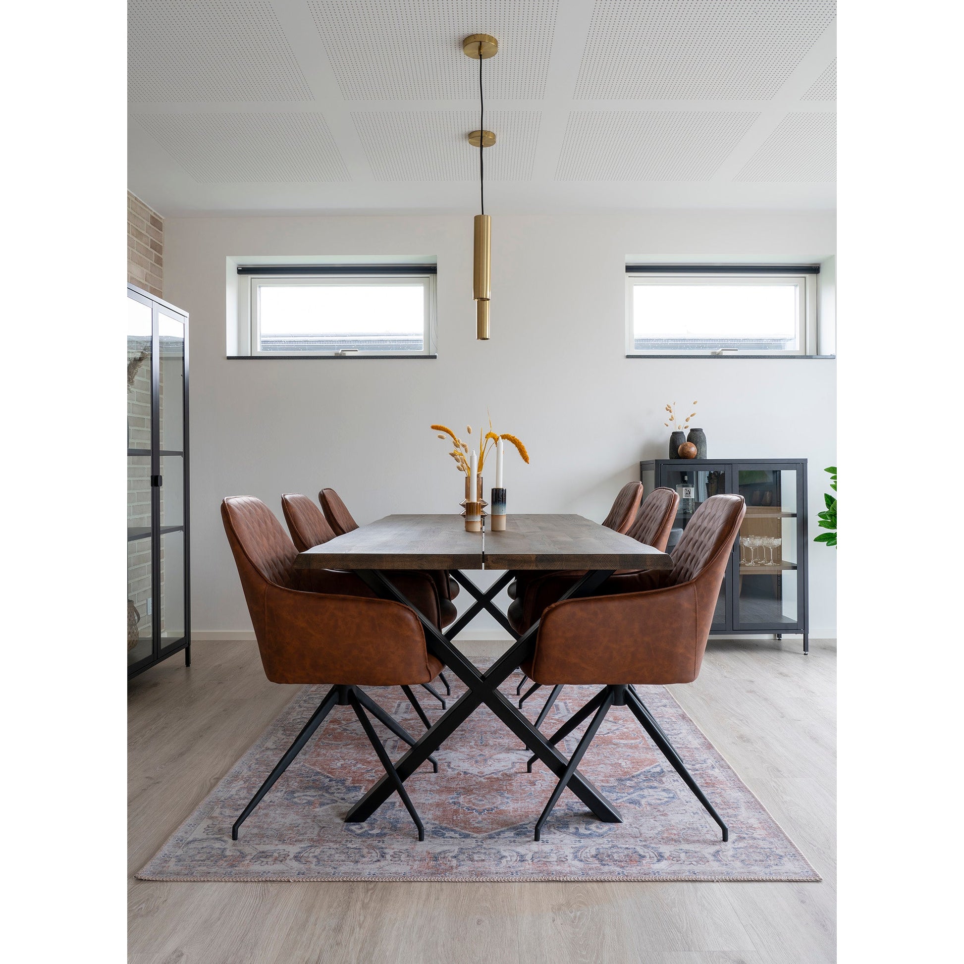 Strakke eethoek met houten tafel, bruine stoelen en stijlvolle hanglamp op vloerkleed in lichte, moderne ruimte.