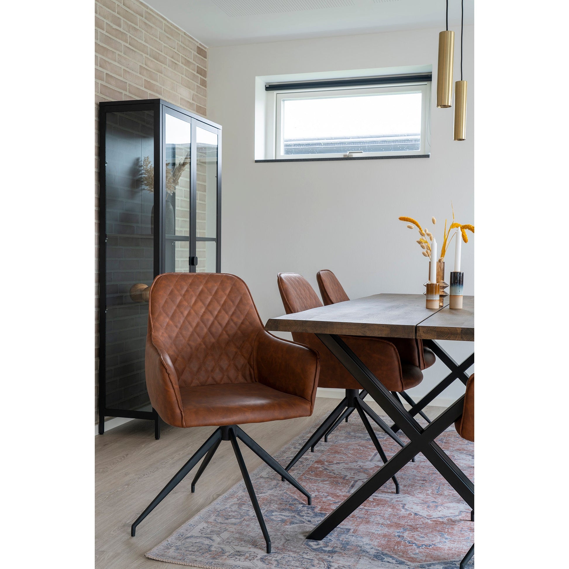 Stijlvolle eetkamer met bruine leren stoelen, houten tafel, vaas met gele bloemen en gouden hanglampen.