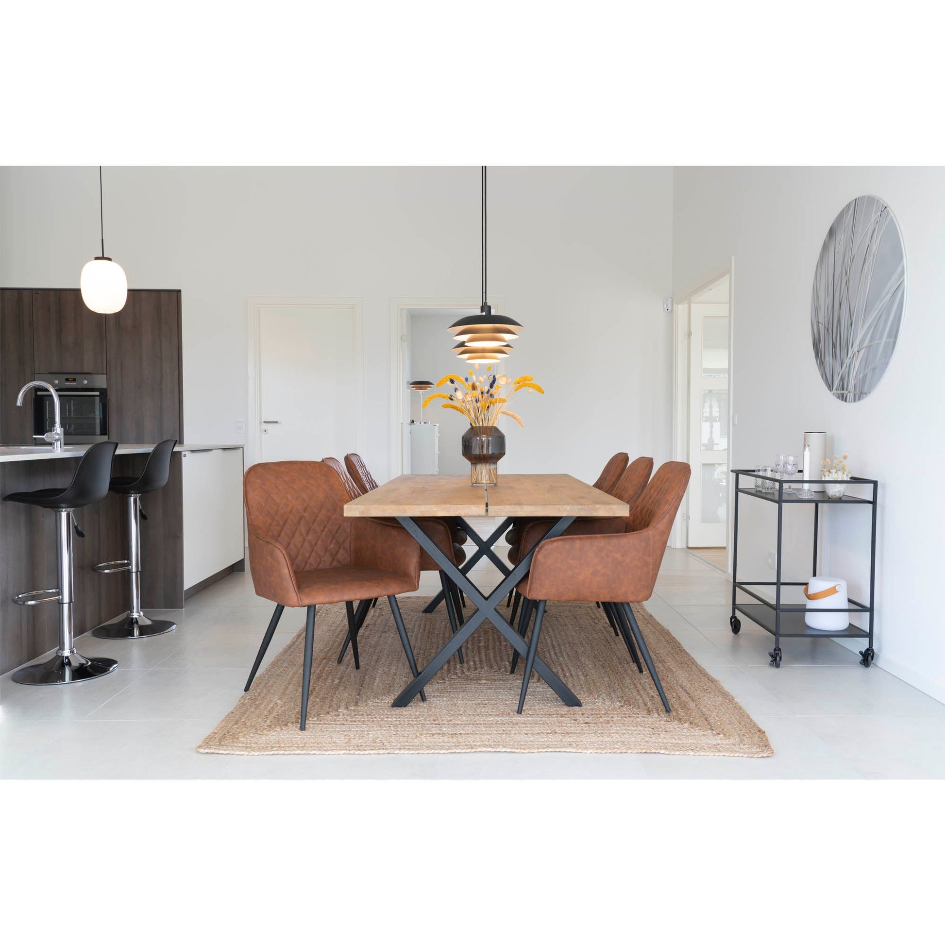 Eetkamer met houten tafel, bruine leren stoelen, moderne hanglamp en decoratie met gele bloemen op beige kleed.