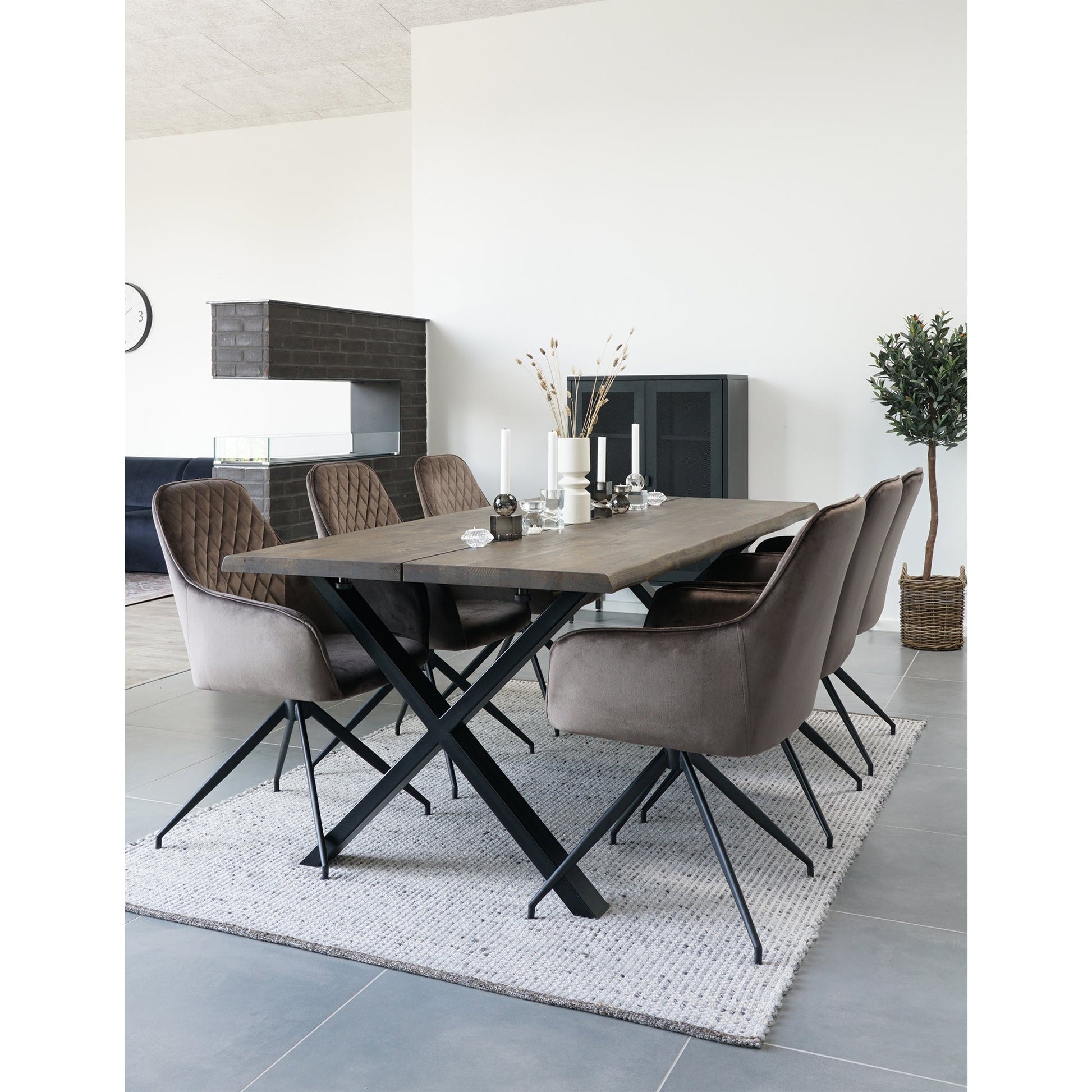 Moderne eetkamer met houten tafel, comfortabele bruine stoelen, kaarsen en een plant in een knusse sfeer.