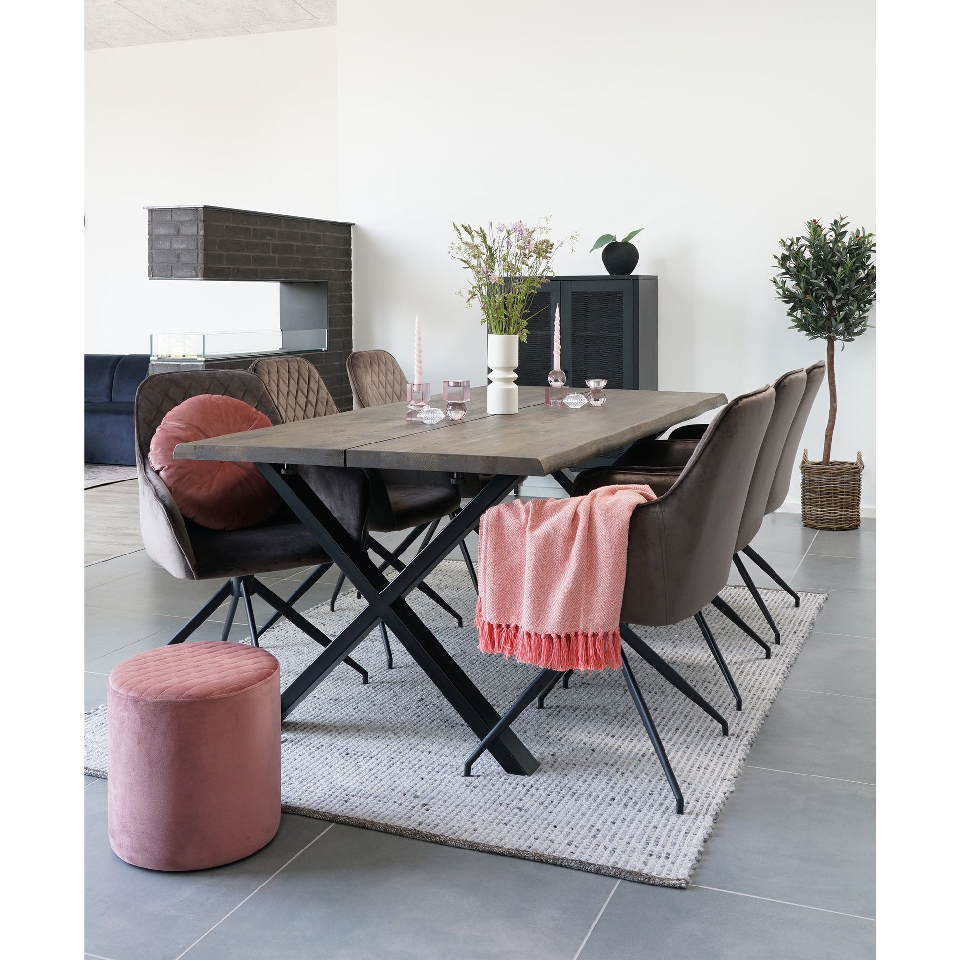 Moderne eetkamer met houten tafel, bruine stoelen, roze accenten en bloemen, op een grijze tegelvloer.