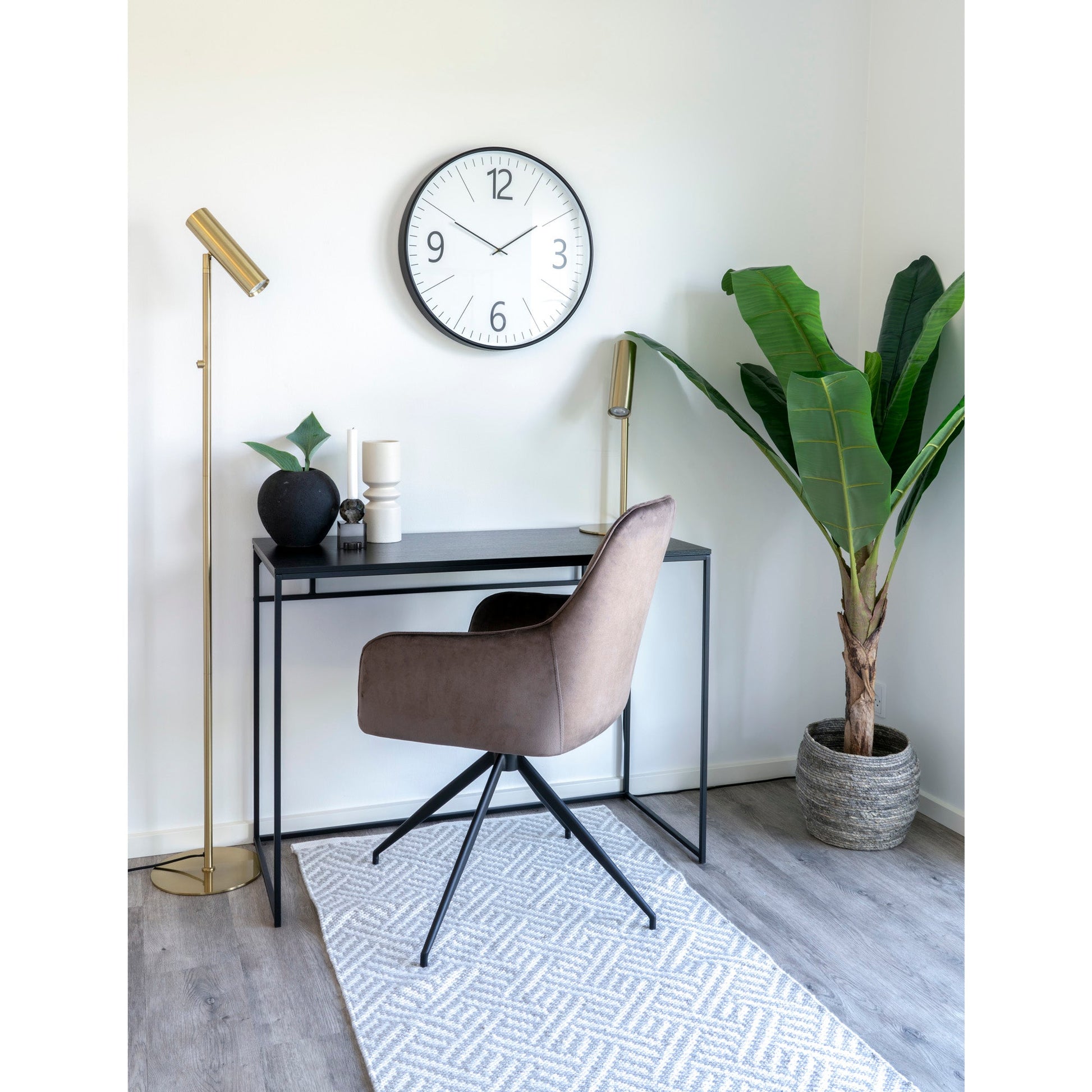 Strakke bureauruimte met bruine stoel, zwarte tafel, grote klok, groene plant en gouden lamp op grijze vloer.
