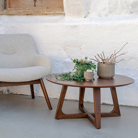 Moderne zithoek met een grijze fauteuil, houten salontafel en planten in keramieken potten tegen witte muur.