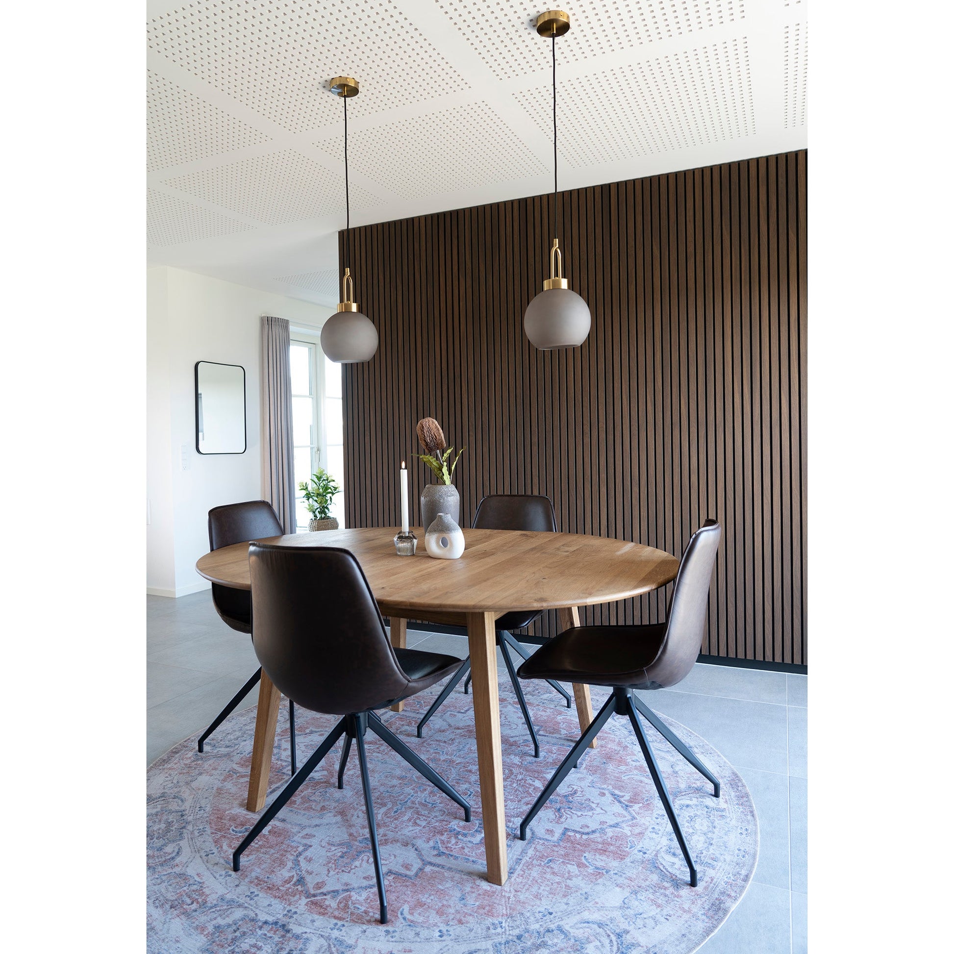 Moderne eetkamer met houten tafel, bruine stoelen, ronde vloerkleed en strakke lampen boven tafel.
