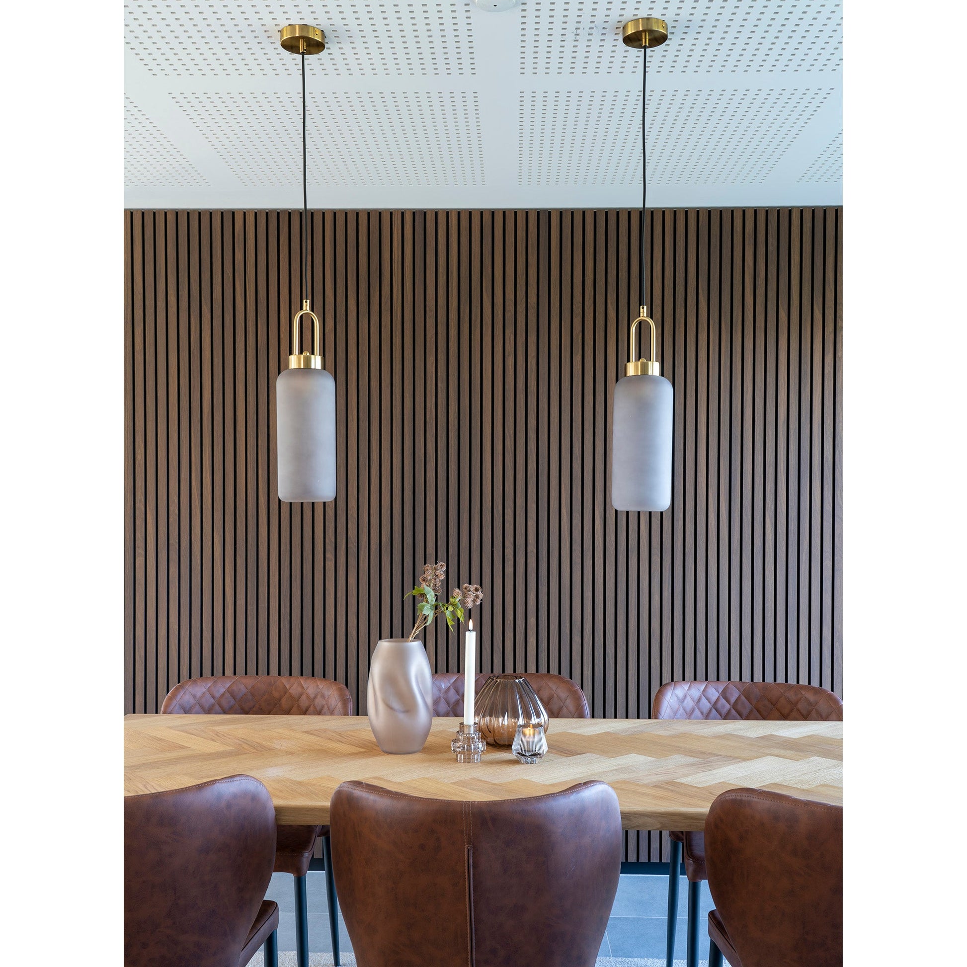 Stijlvolle eetkamer met leren stoelen, houten tafel, vaas en twee hanglampen voor een houten lamellenwand.