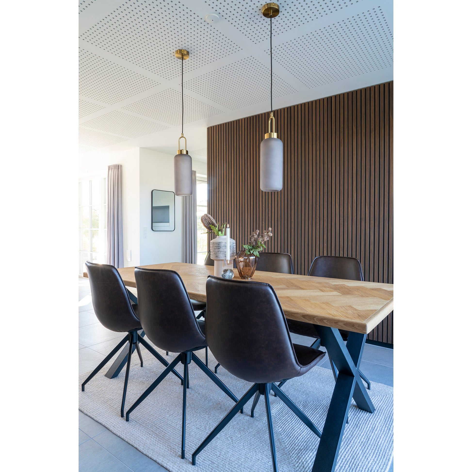 Hedendaagse eetkamer met houten tafel, bruine leren stoelen en moderne hanglampen, tegen een wand van houten latten.