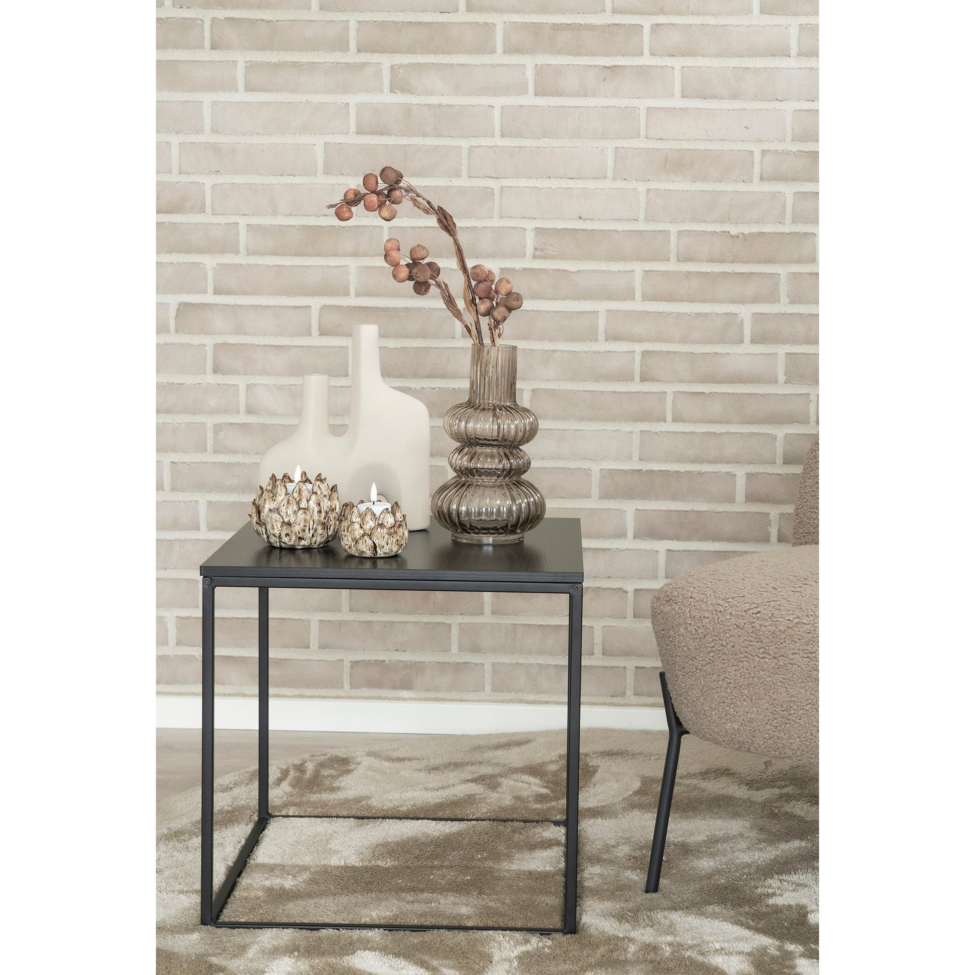 Stijlvolle bijzettafel met decoratieve vazen en kandelaars tegen een beige bakstenen muur.