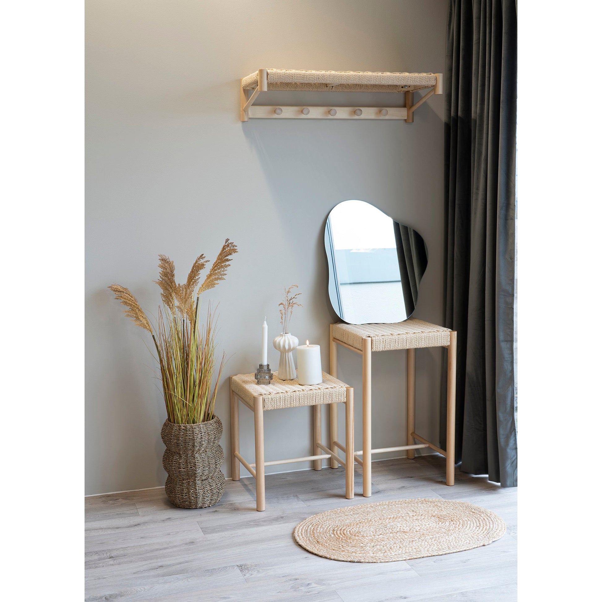 Scandinavische hal met houten meubels, rieten mand met gras, twee kaarsen en een organisch gevormde spiegel.