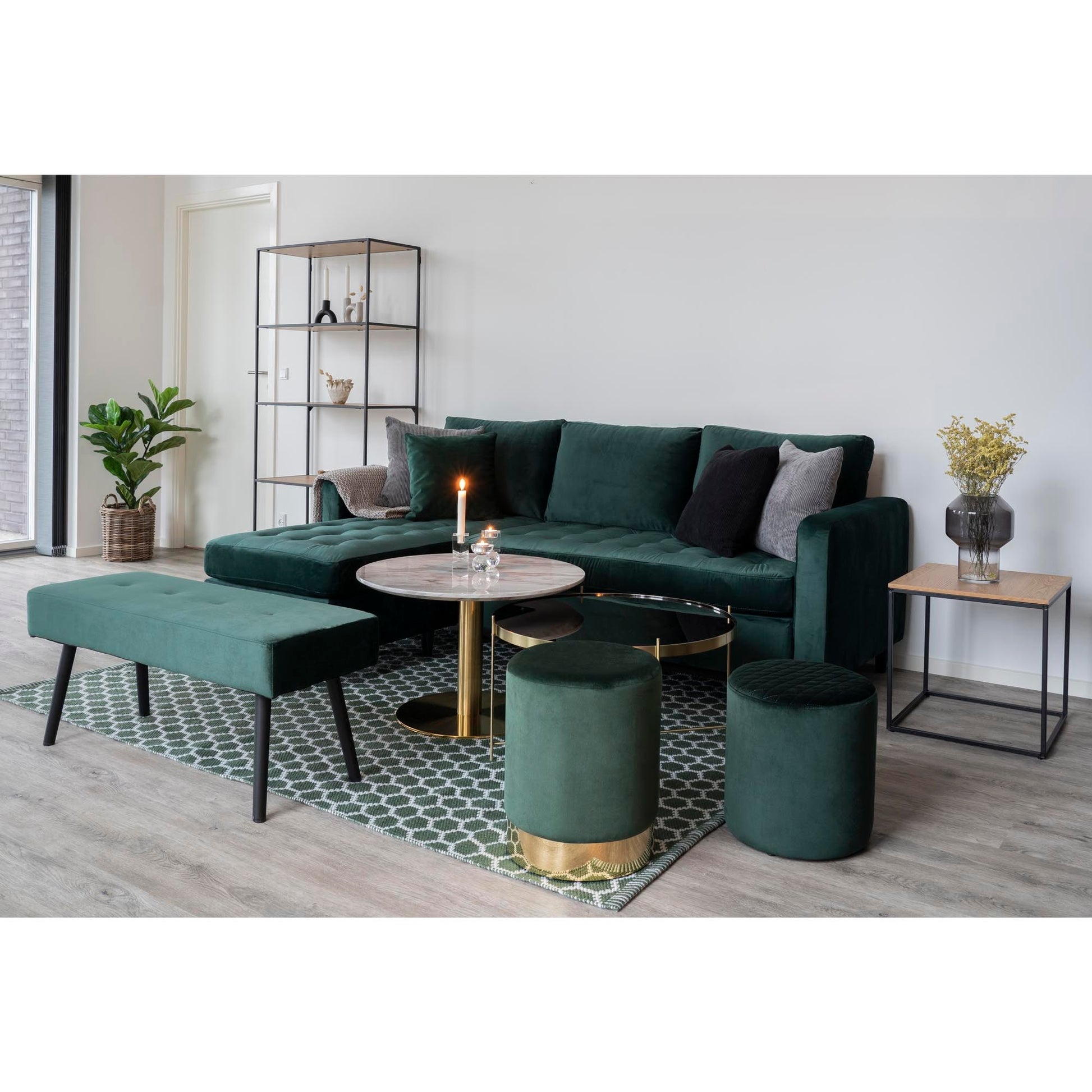 Stijlvolle woonkamer met donkergroene fluwelen bank, ronde bijzettafels, planten en kaars in een moderne sfeer.