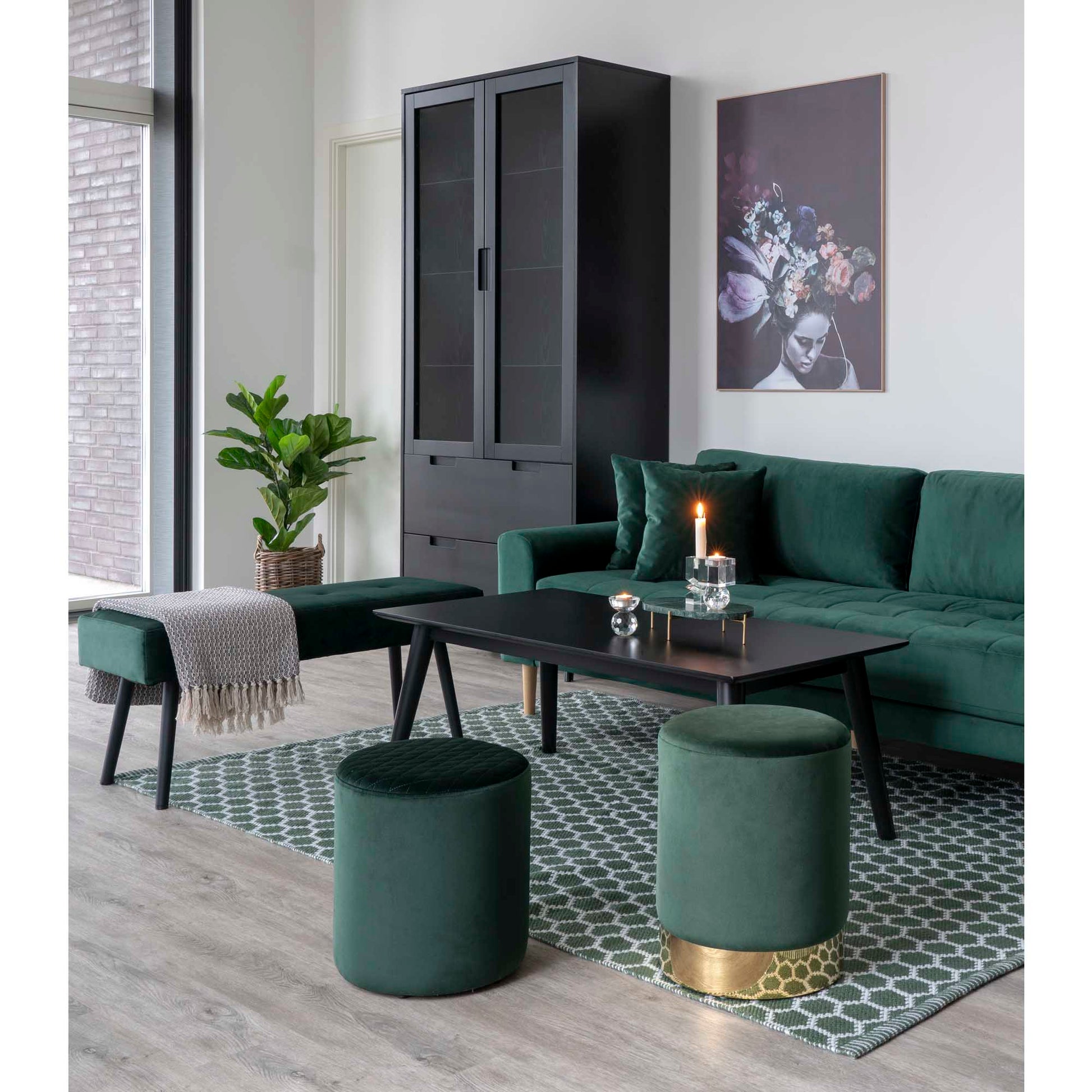 Stijlvolle woonkamer met donkergroene fluwelen bank, salontafel, plant, kunst aan de muur en een brandende kaars.