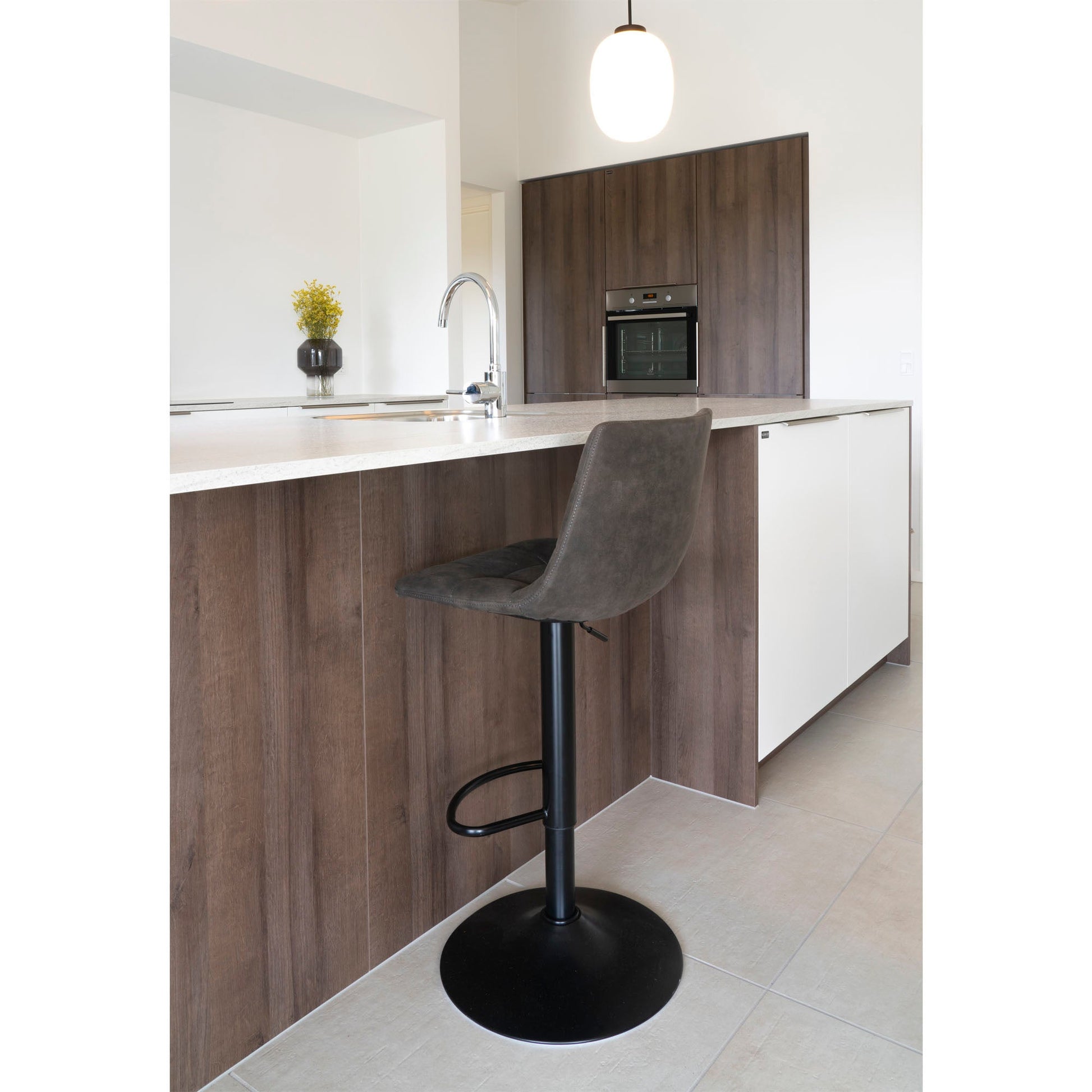 Moderne keuken met donkerhouten fronten, beige aanrechtblad, hoge grijze kruk en hanglamp.