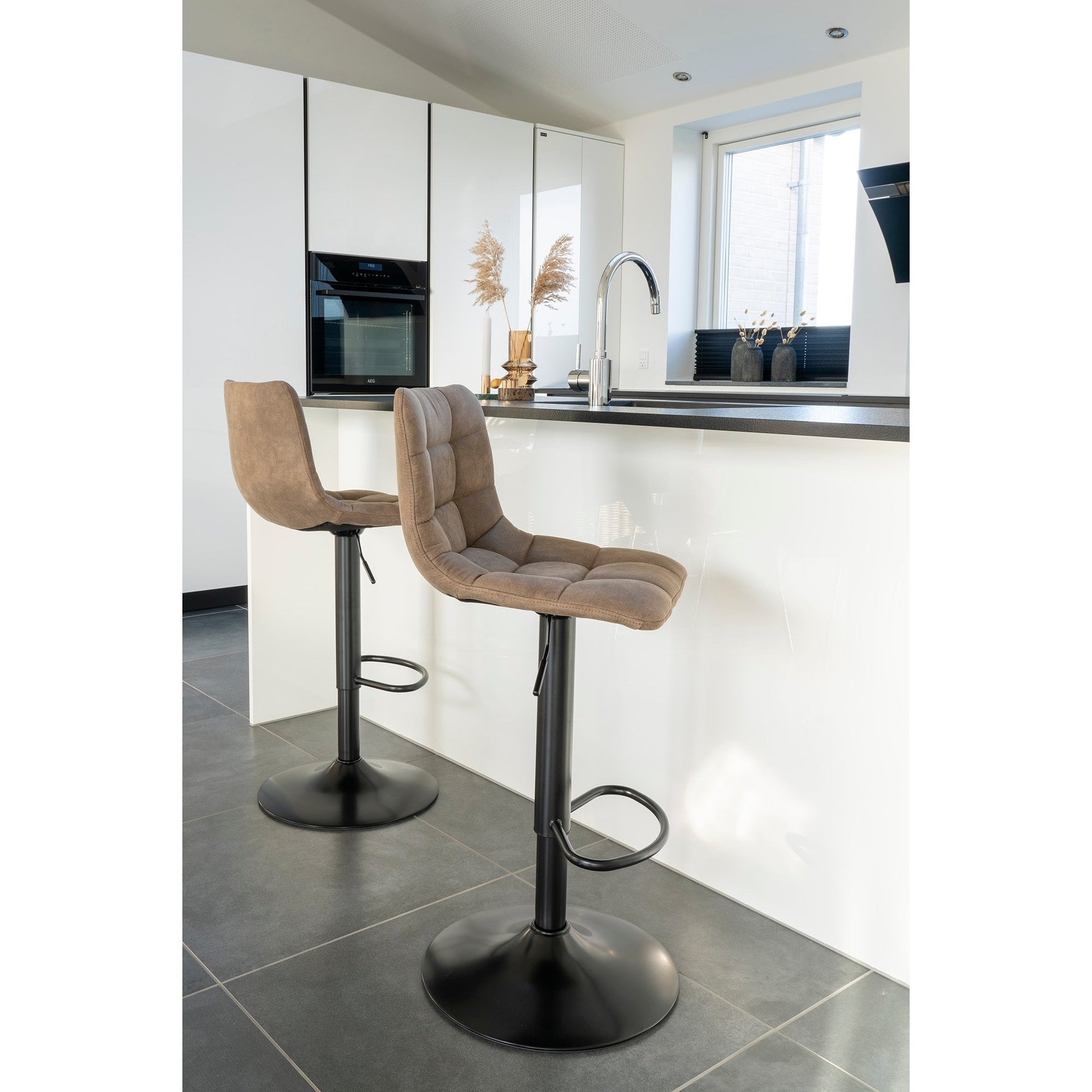 Twee beige barkrukken met zwarte voetstukken bij een modern witte keuken met spiegelkast en kraan.