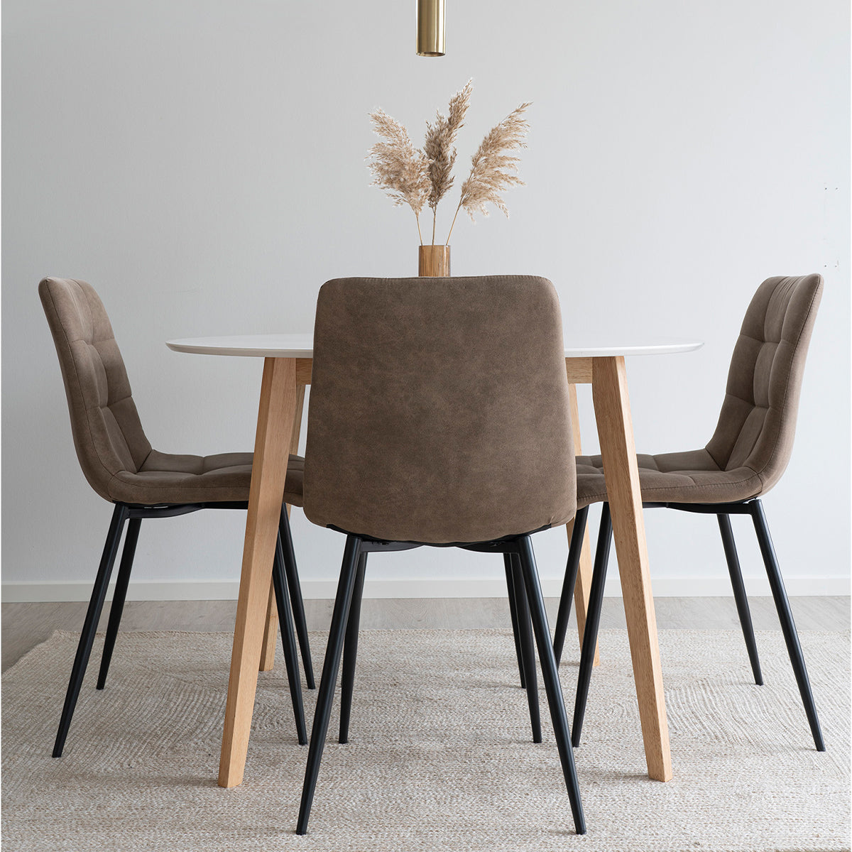 Moderne eetkamerset met vier bruine stoelen, een ronde witte tafel en een vaas met pampasgras op een tapijt.