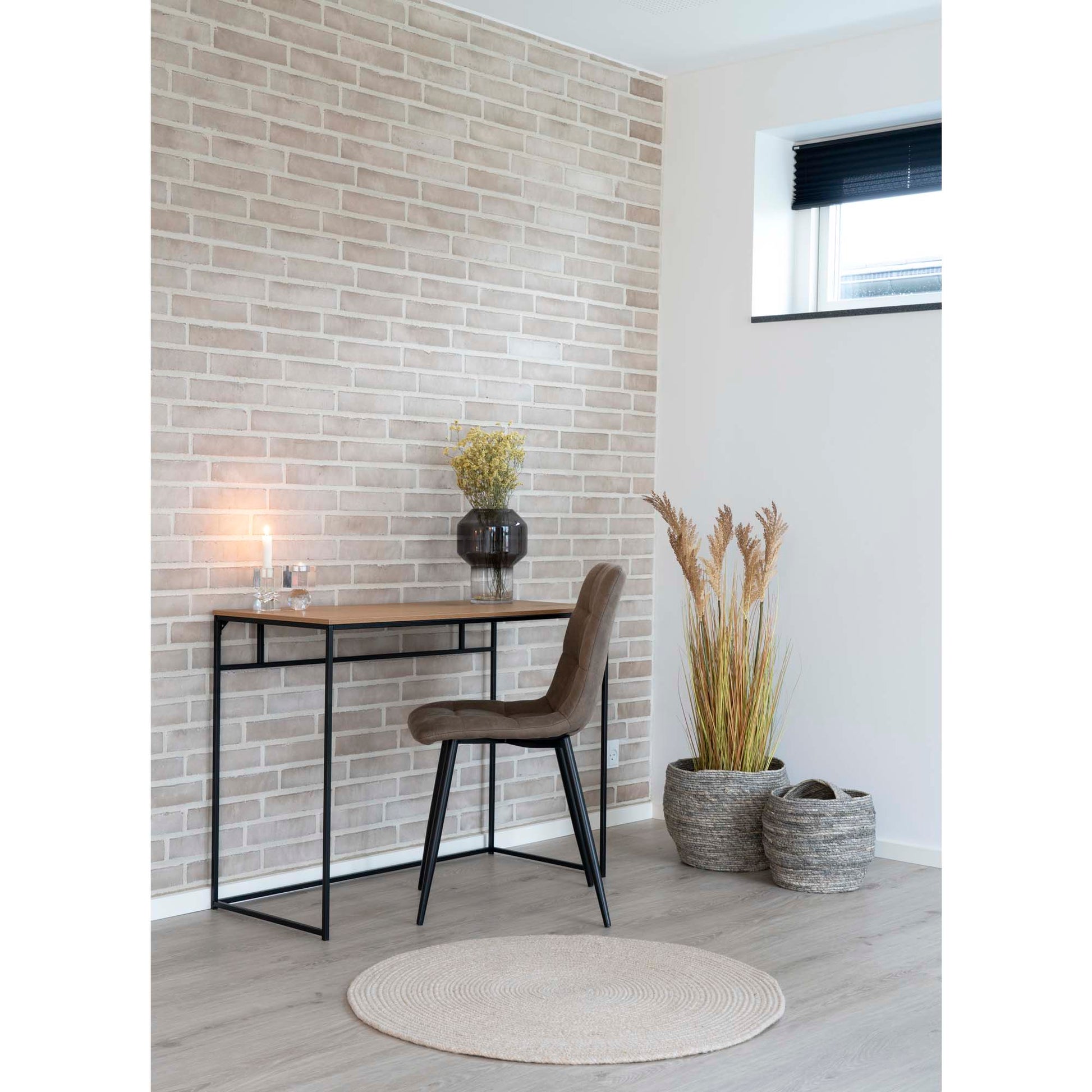 Stijlvolle werkplek met houten bureau, bruine stoel, vaas met bloemen en warme verlichting voor bakstenen muur.
