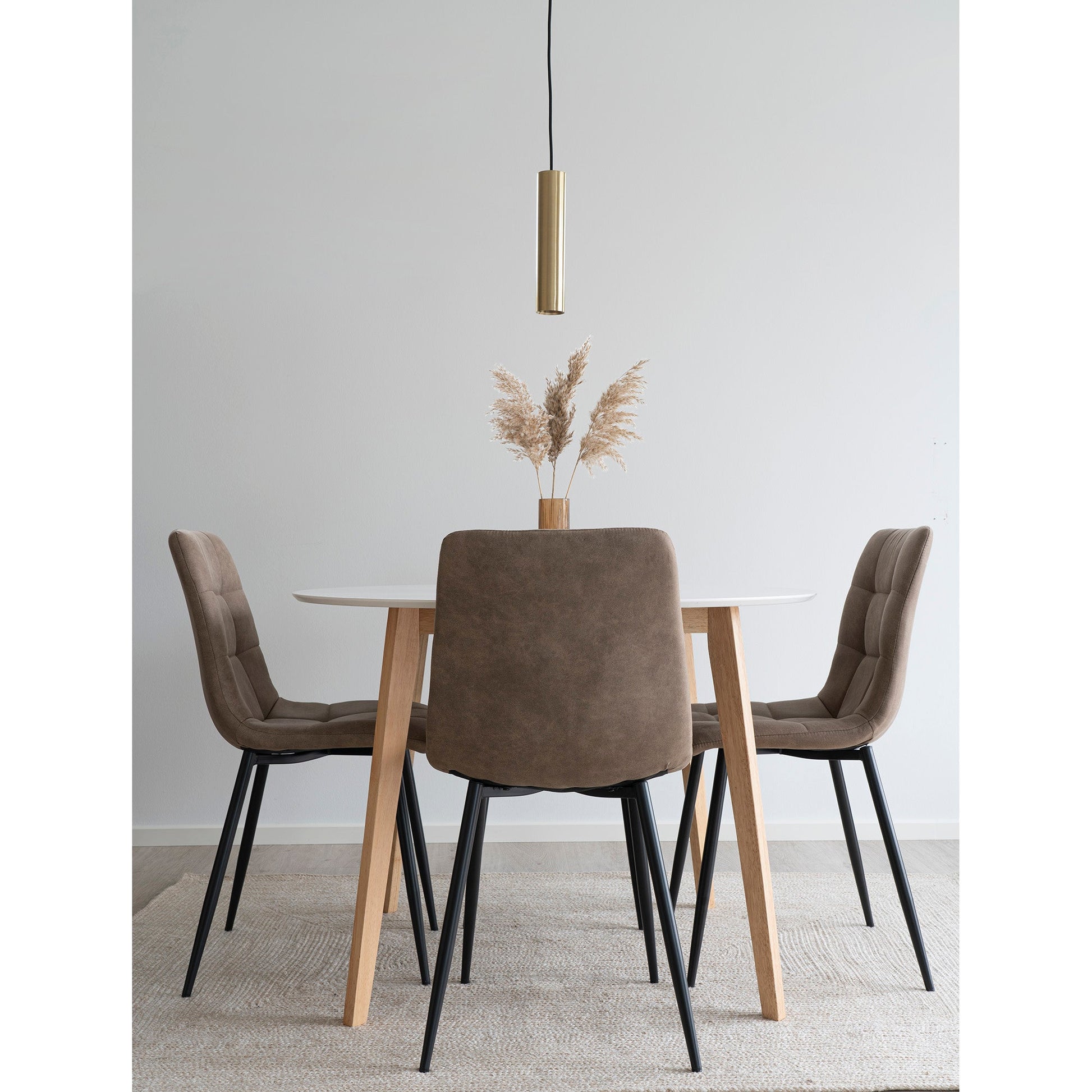 Minimalistisch eetkamerinterieur met ronde tafel, bruine stoelen, pampasgras en een gouden hanglamp.