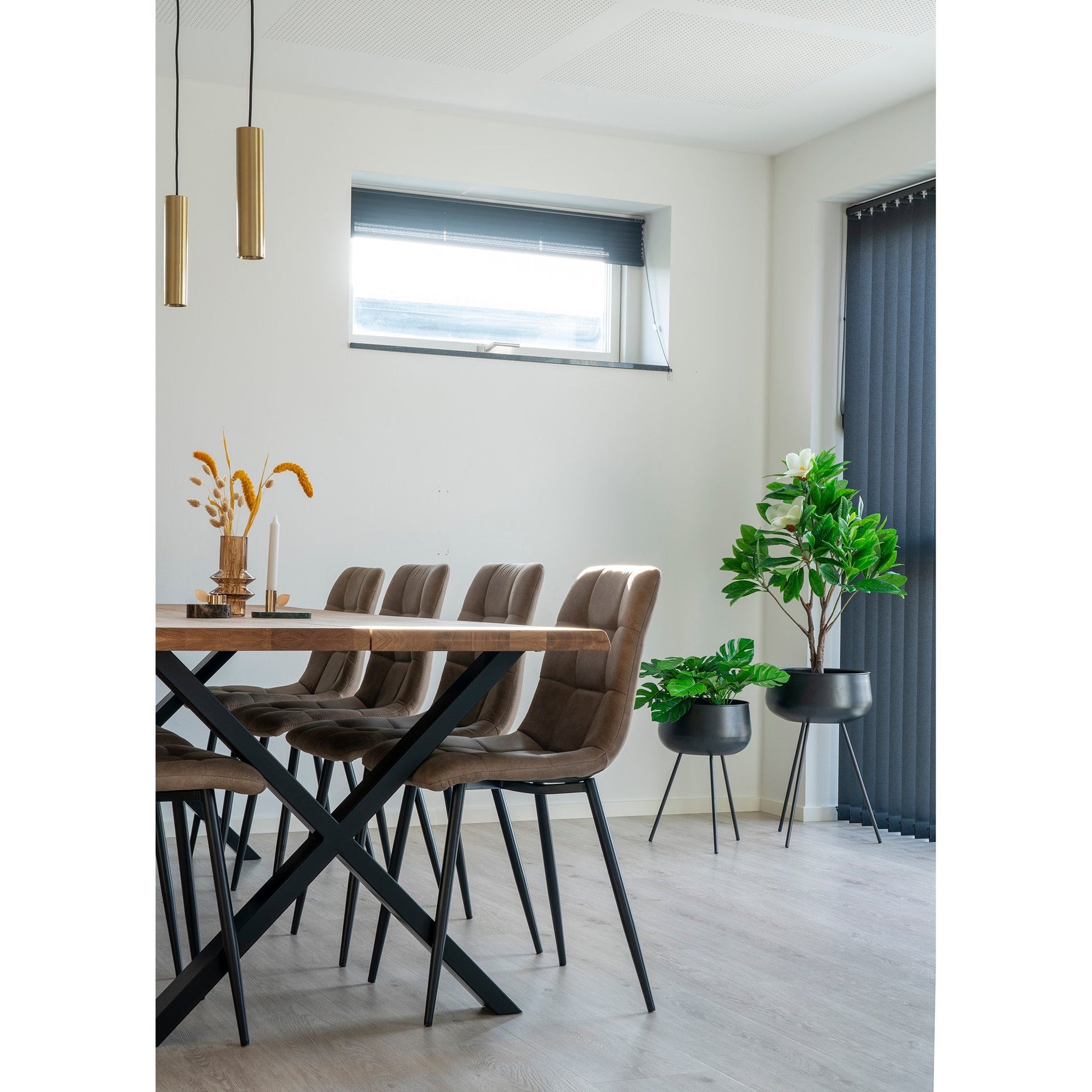 Moderne eetkamer met houten tafel, zes bruine stoelen, gouden hanglampen en groene planten in potten.