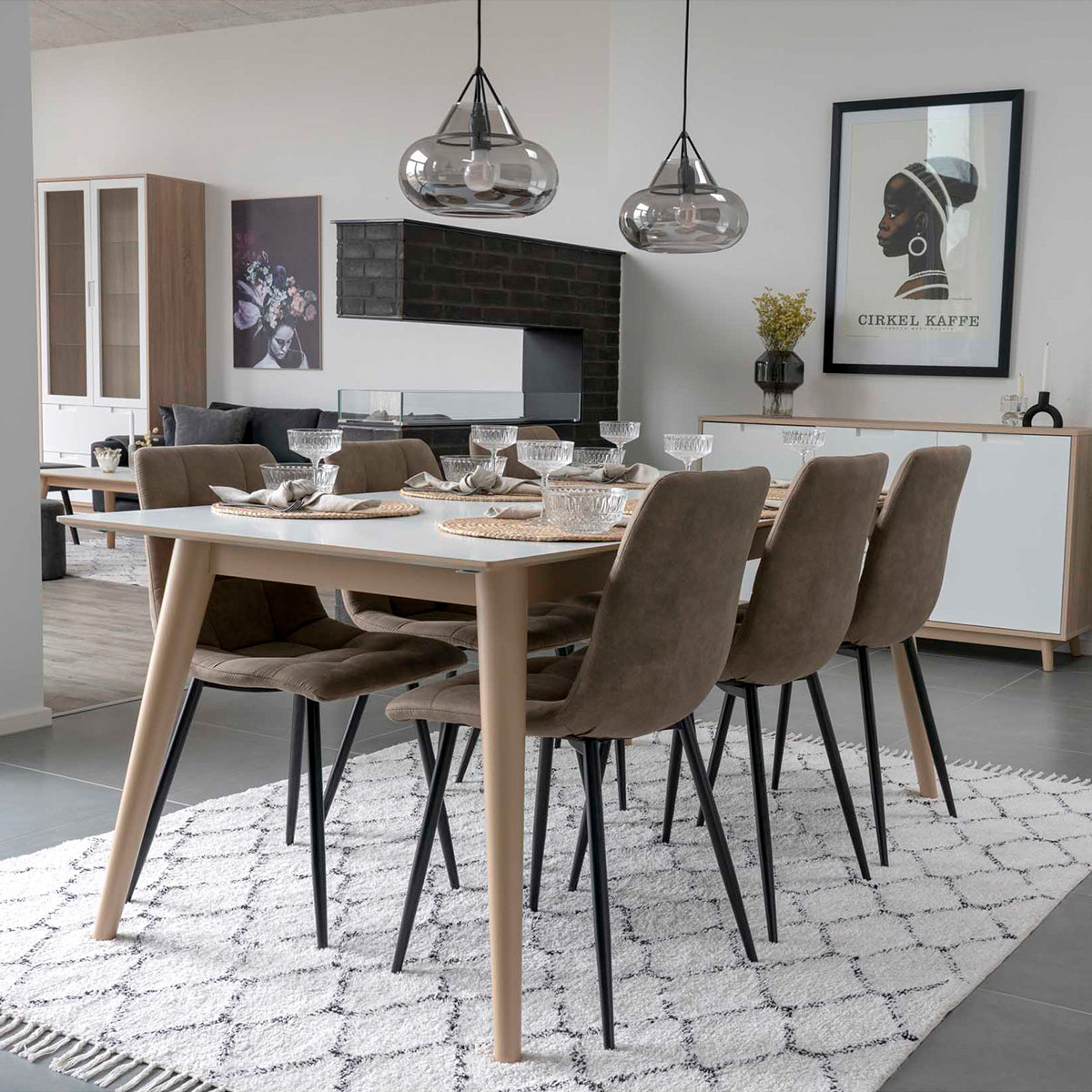 Eetkamer met moderne houten tafel, zes bruine stoelen, glazen lampen en kunstwerk met tekst 'CIRKEL KAFFE'.