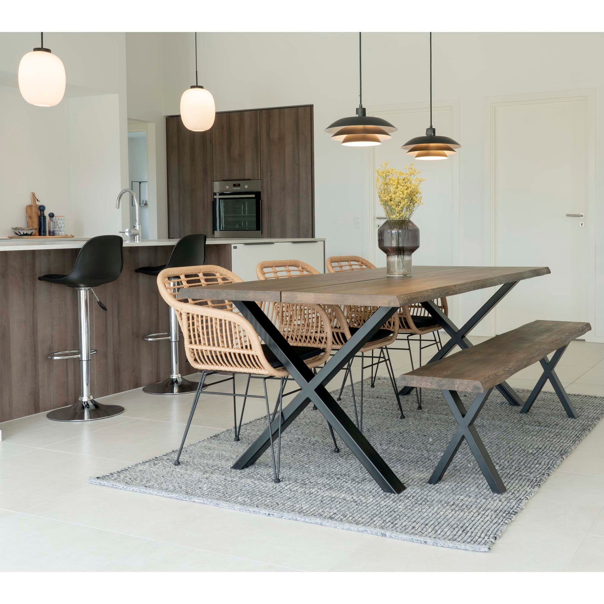 Moderne eetkamer met houten tafel, rieten stoelen en bankje, hangende lampen en keukenbar met krukken.