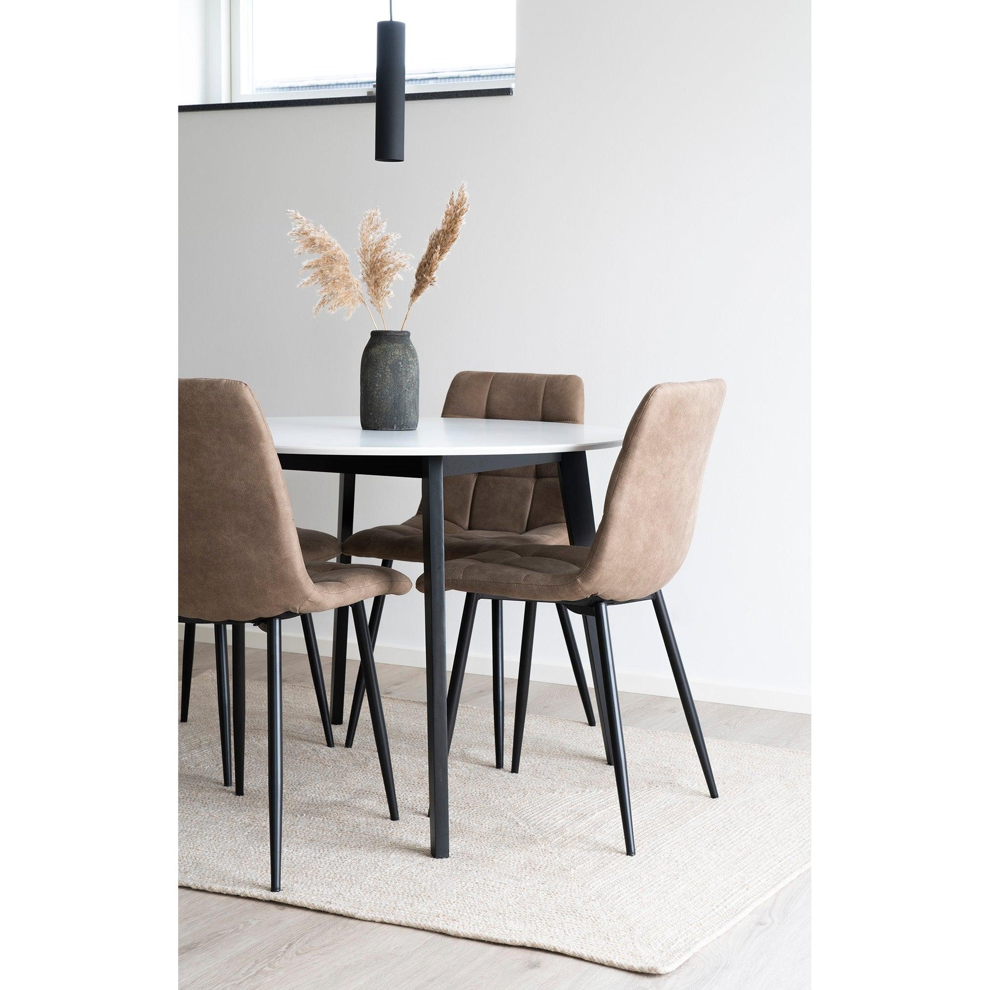 Stijlvolle eetkamerset met wit tafelblad, bruine stoelen en vaas met pampagrassen op beige tapijt.