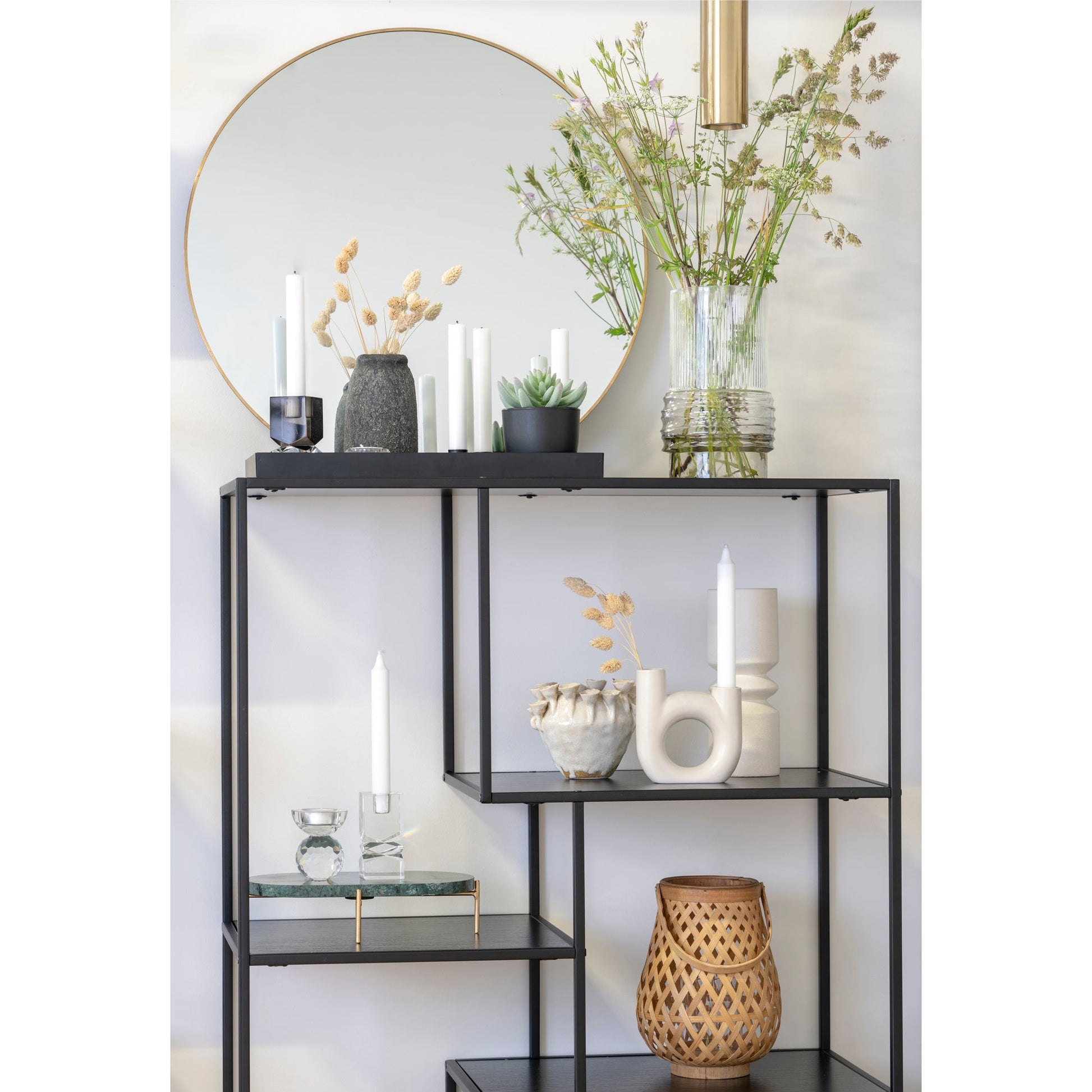 Zwart rek met decoratieve vazen, kaarsen en planten voor een grote ronde spiegel met goudrand.