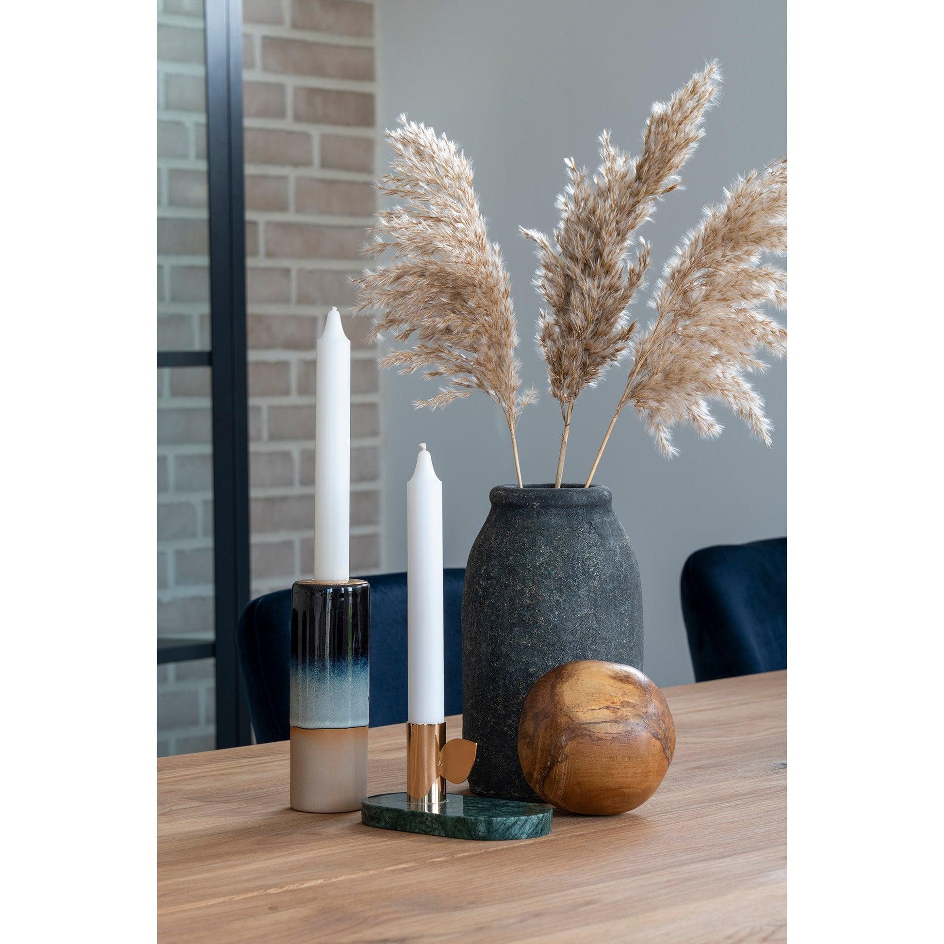 Stijlvolle tafelopstelling met gedroogd siergras in een vaas, kaarsen, en een houten decoratie op eiken tafel.