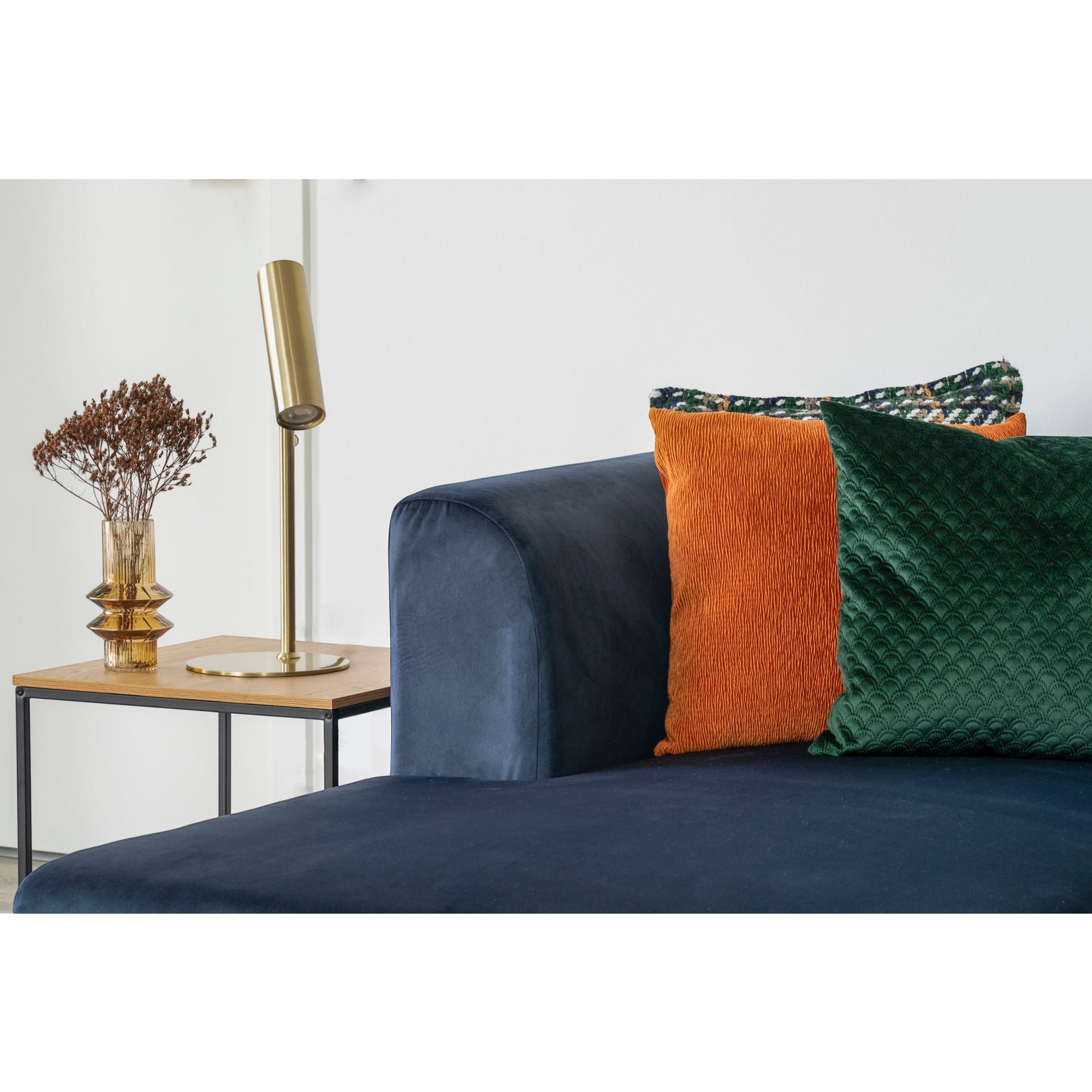 Scandinavische woonkamer met Vita bijzettafel van House Nordic naast smaragdgroene bank en open wandrek.