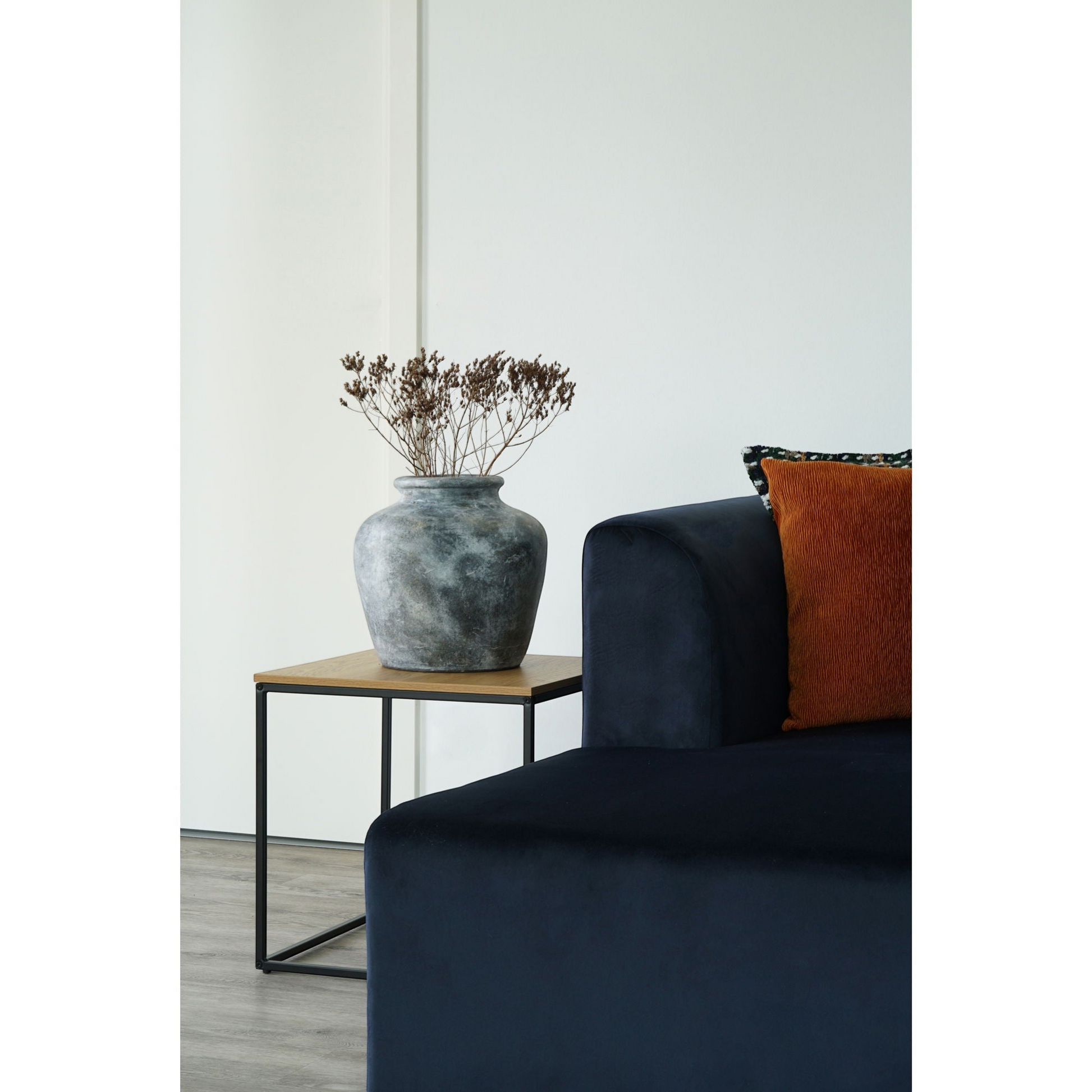 Vita bijzettafel van House Nordic naast blauwe sofaarm met kussens, met gouden tafellamp en amberkleurige vaas.