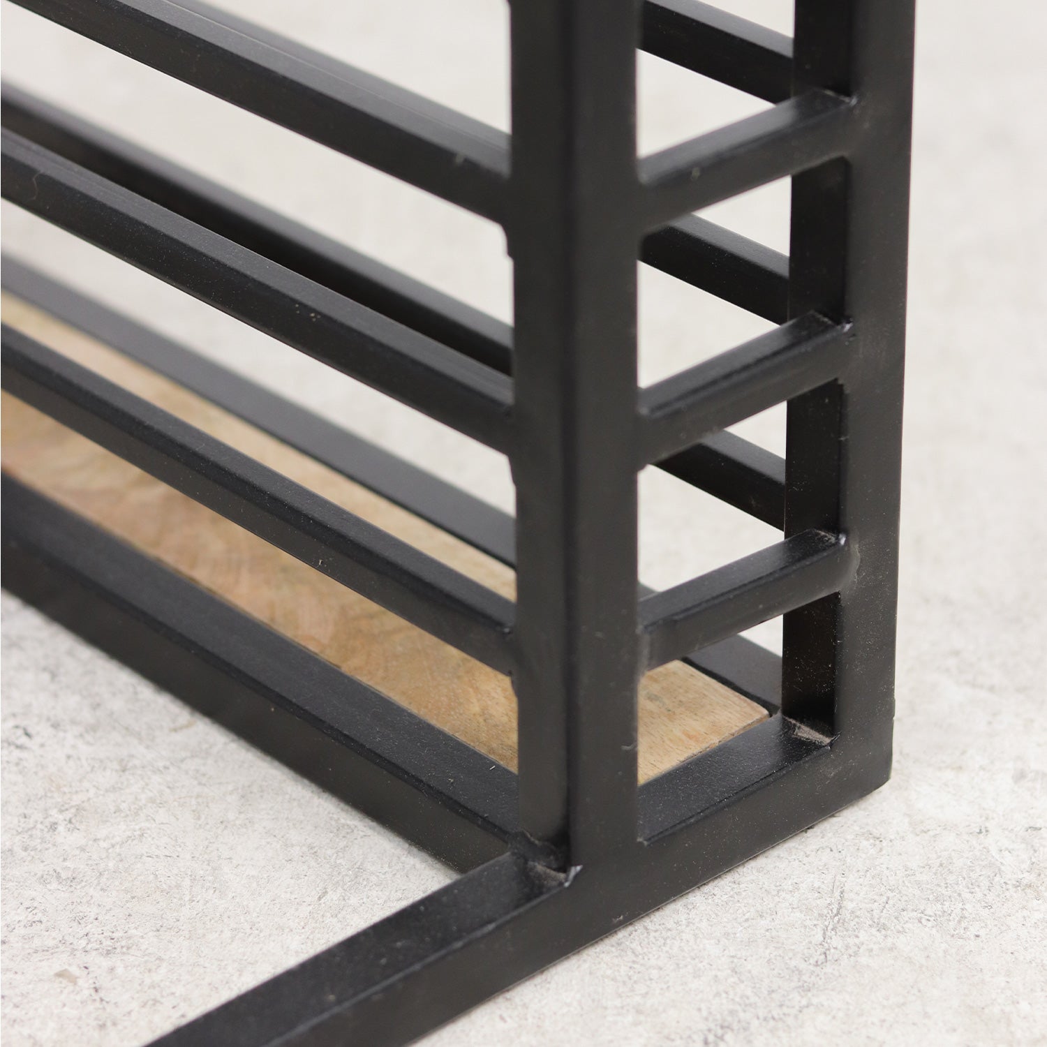 Zwart metalen frame met houten plank, minimalistisch ontwerp, op lichte betonachtige ondergrond.