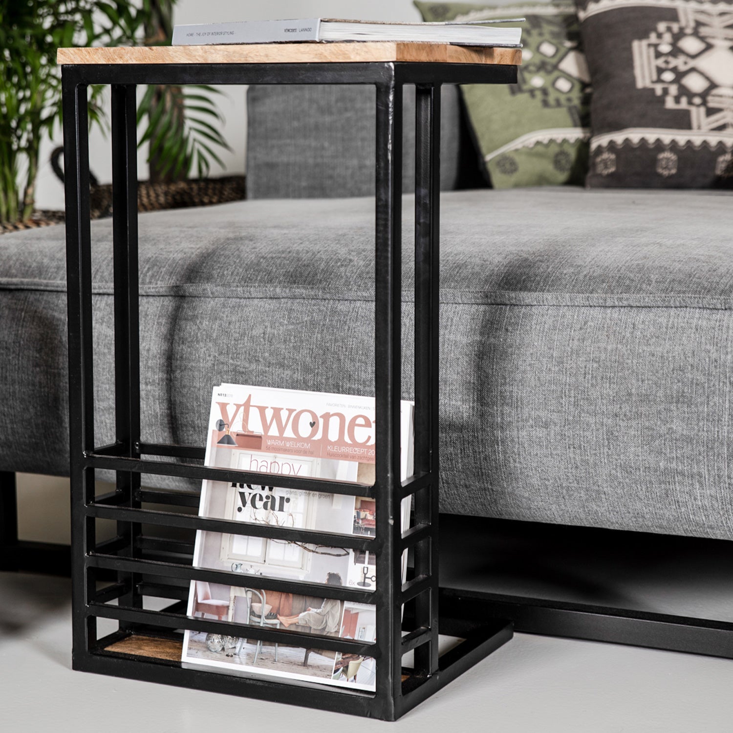 Industriële bijzettafel met onderin tijdschrift "vtwonen", naast een grijze bank en groene sierkussens.