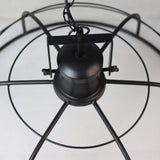 Zwarte industriële hanglamp met metalen frame en rustieke ketting tegen een lichte achtergrond.