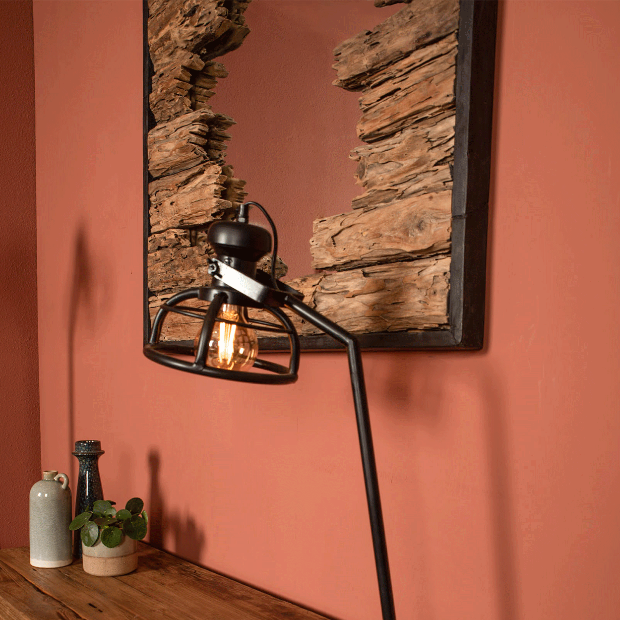 Industriële lamp met gloeilamp en spiegel met houtaccenten tegen roestbruine muur, rustieke sfeer.