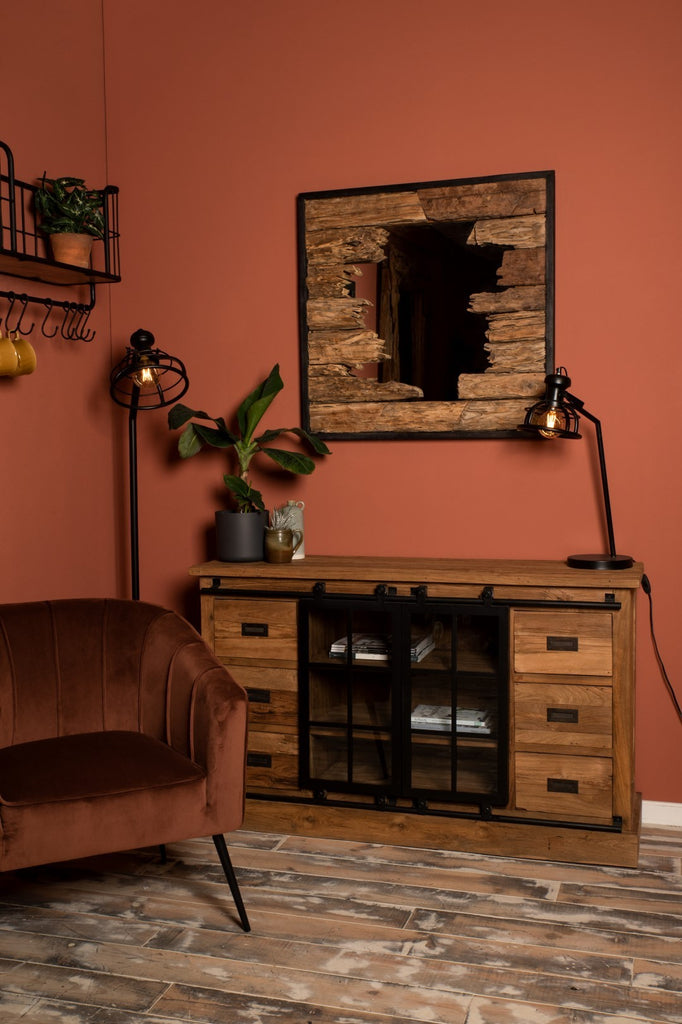 Gezellige woonkamer met roestkleurige muur, houten dressoir, fluwelen stoel en industrieel verlichte hoek.