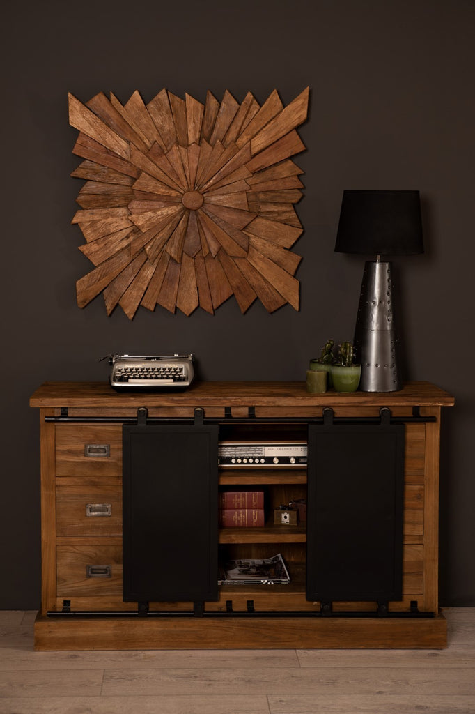 Houten dressoir met typemachine, decoratieve metalen lamp en wandkunst op een donkere muur.