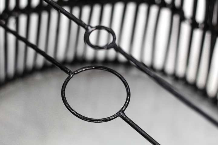 Zwarte metalen mand met cirkelvormige details tegen een vervaagde achtergrond, minimalistisch ontwerp.