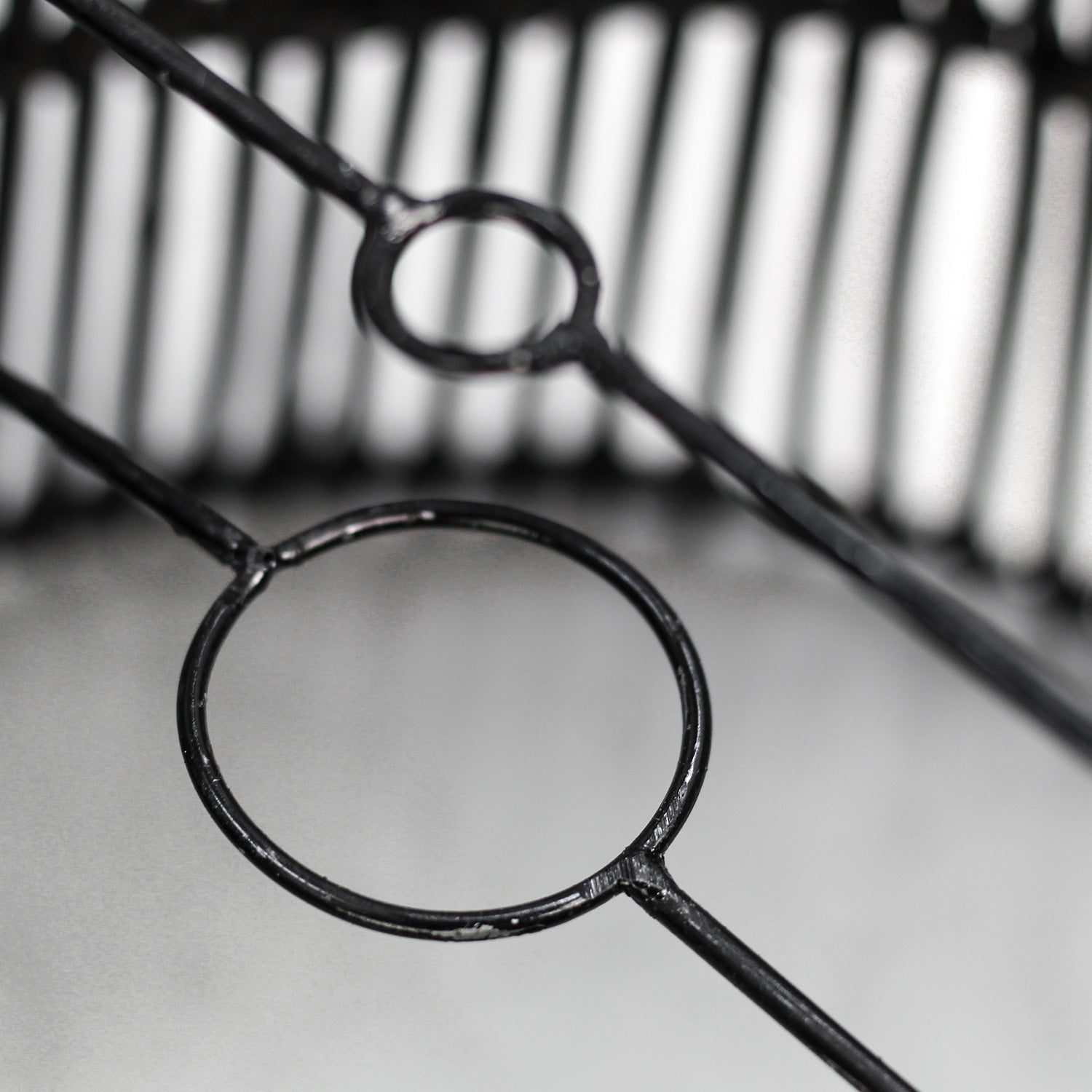 Zwart metalen rasterwerk met cirkelvormige patronen, scherp in contrast tegen een wazige, grijze achtergrond.