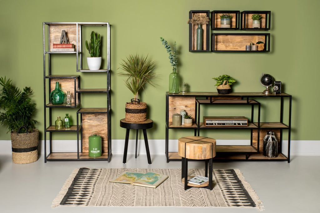 Stijlvolle huiskamer met houten en metalen meubels, groene planten en aardetinten tegen een olijfgroene muur.
