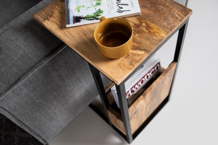 Houten bijzettafel met gele mok, tijdschrift “FLOWERS” en boek met groene plantenfoto naast een grijze bank.