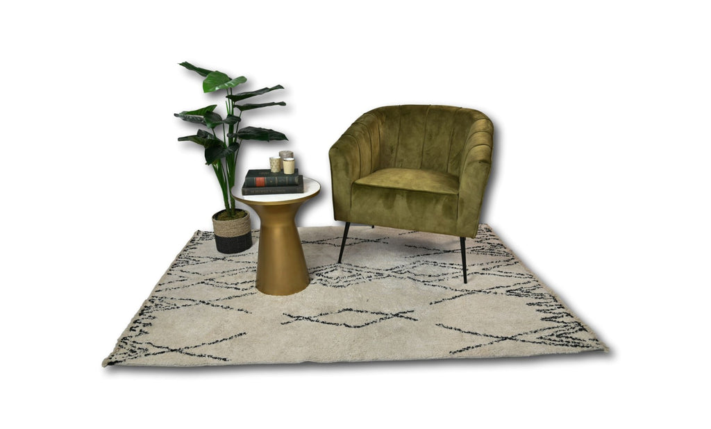 Groene fluwelen stoel naast een gouden bijzettafel met boeken, kaarsen, plant op een crèmekleurig tapijt.
